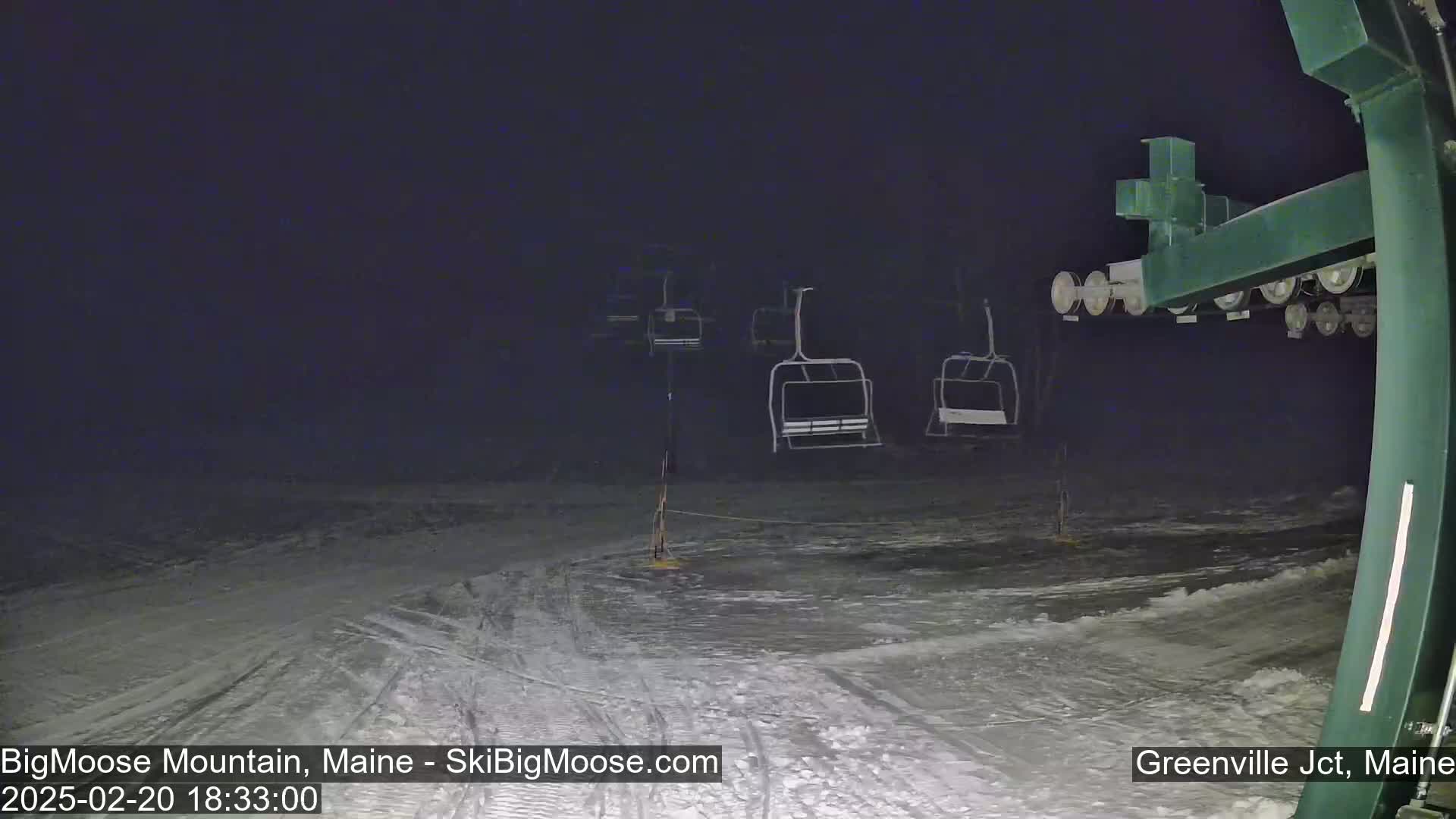 A nighttime view of a snow-covered ski slope with several empty chairlifts under dark skies.