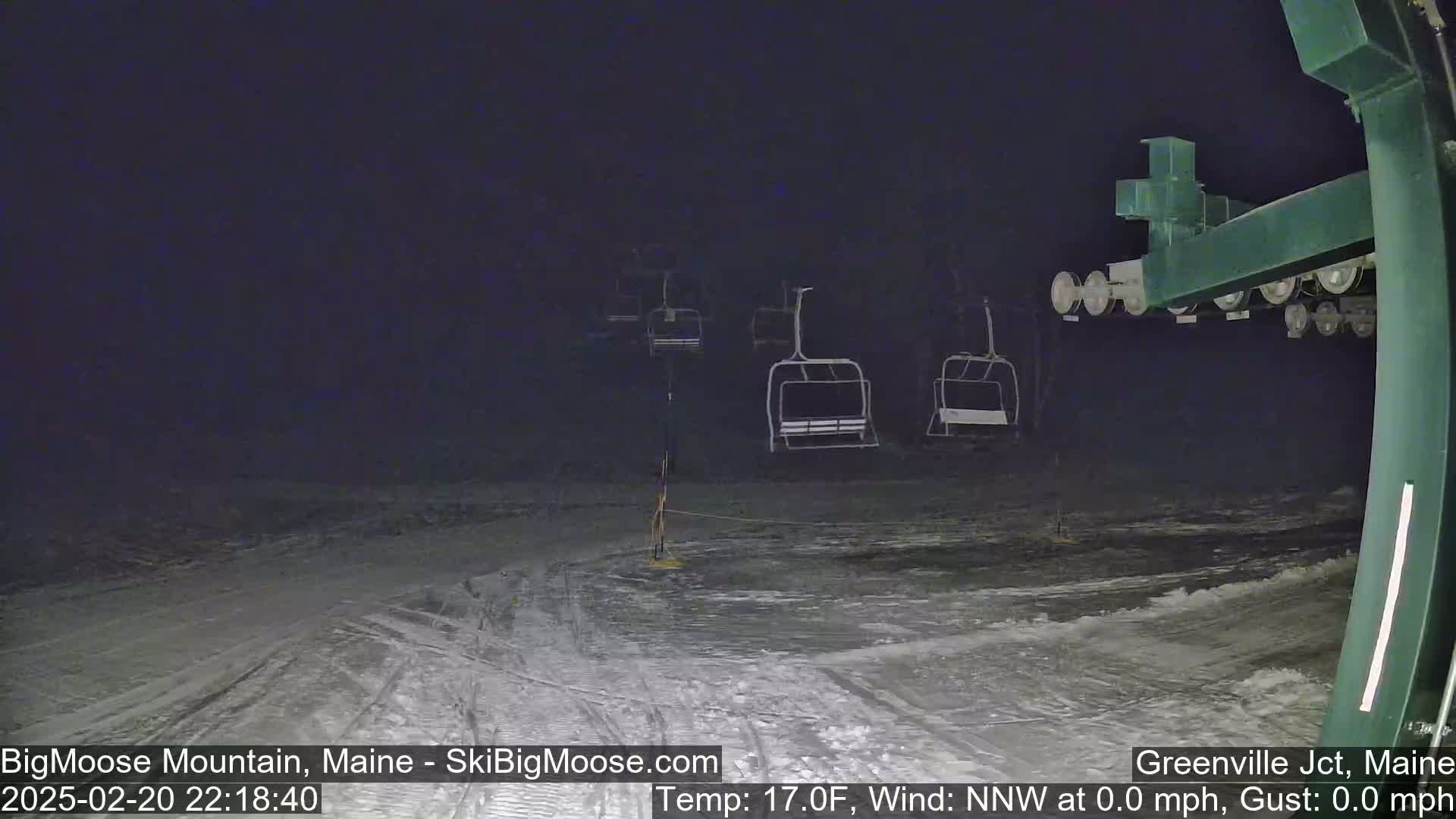 A nighttime view of a snow-covered ski slope with empty chairlifts under a dark sky.