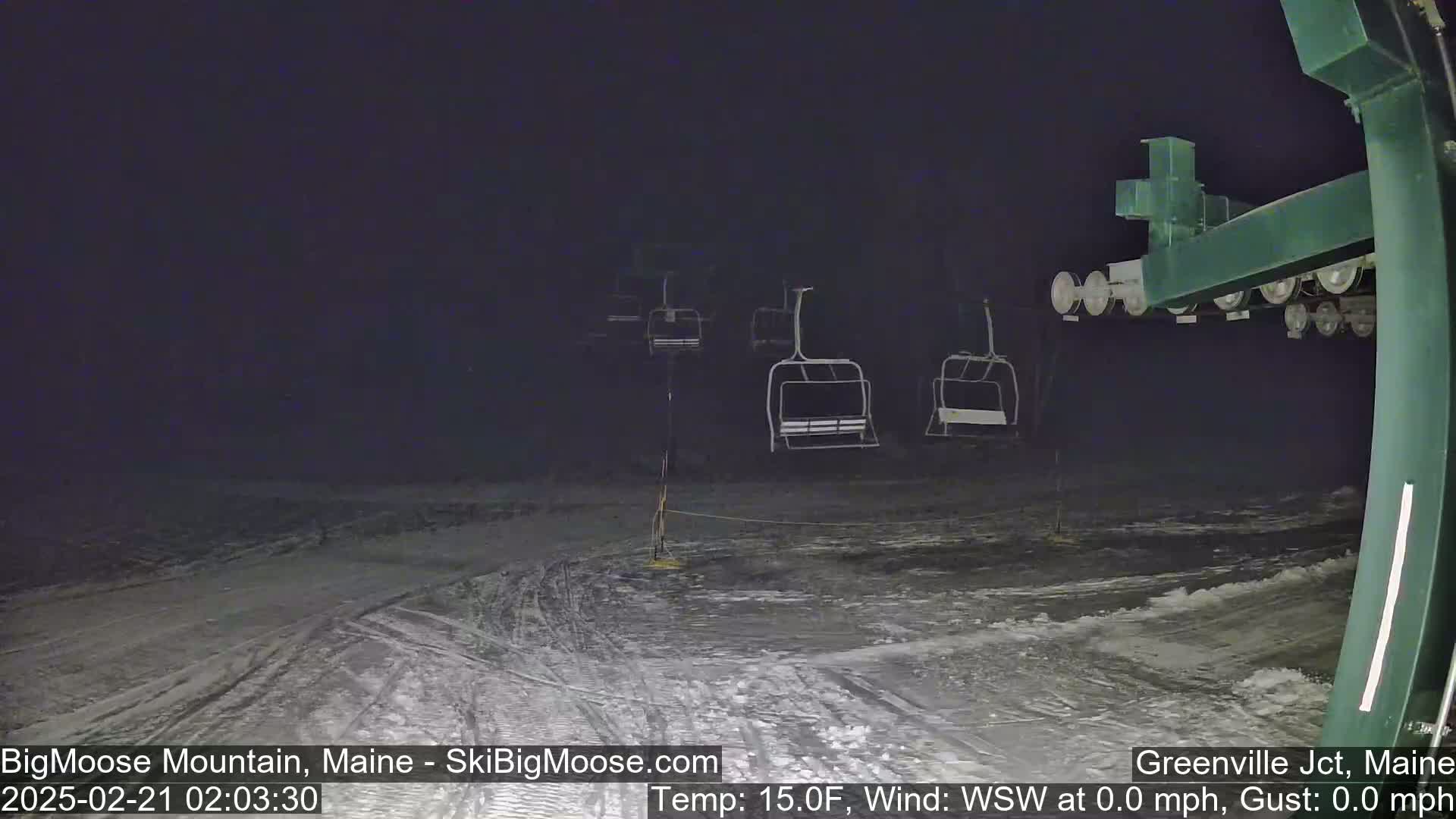 A nighttime view of a snow-covered ski slope with empty chairlifts under a dark sky.
