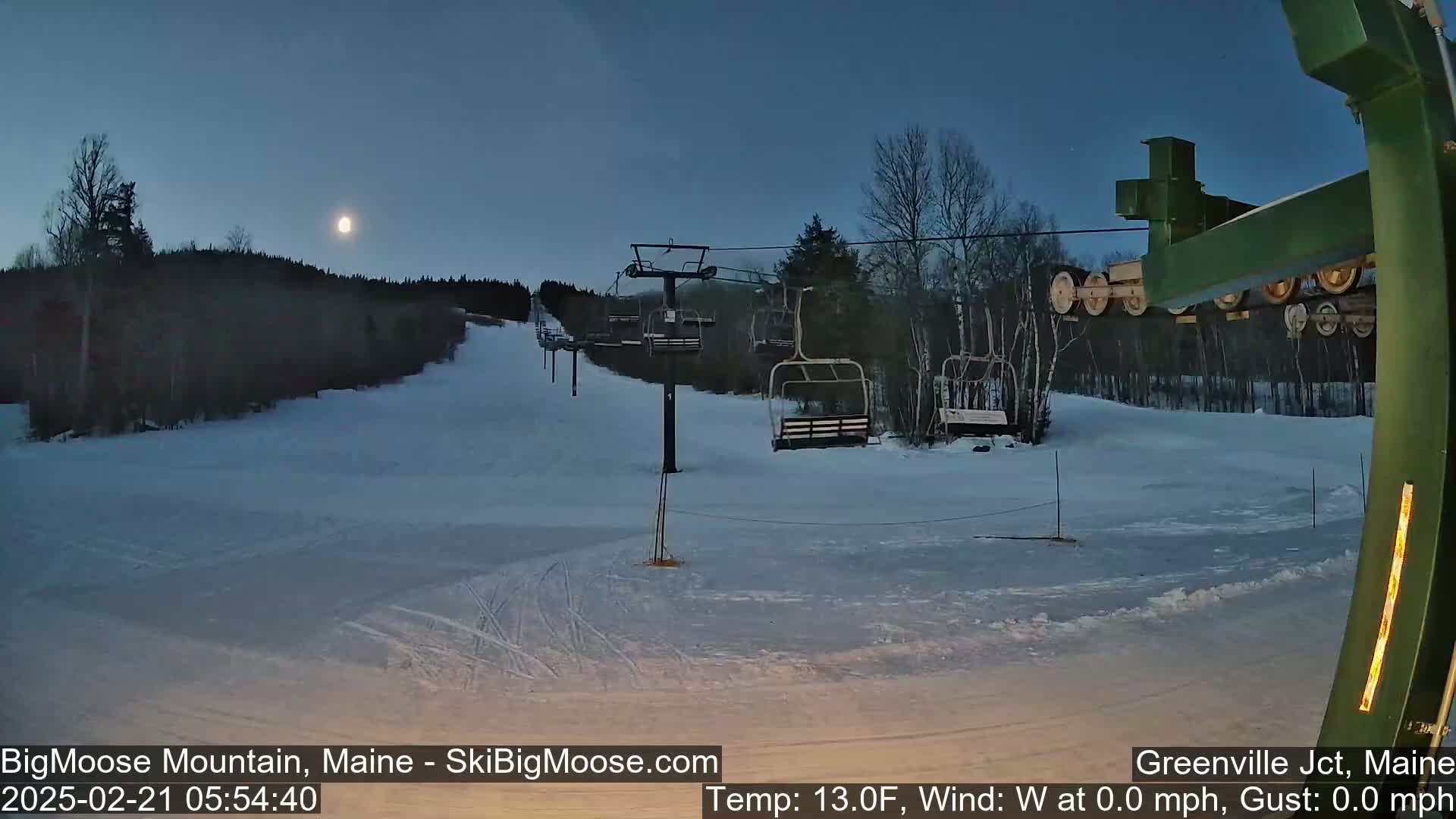 A moonlit ski slope with a chairlift and snow-covered trees under a clear night sky.