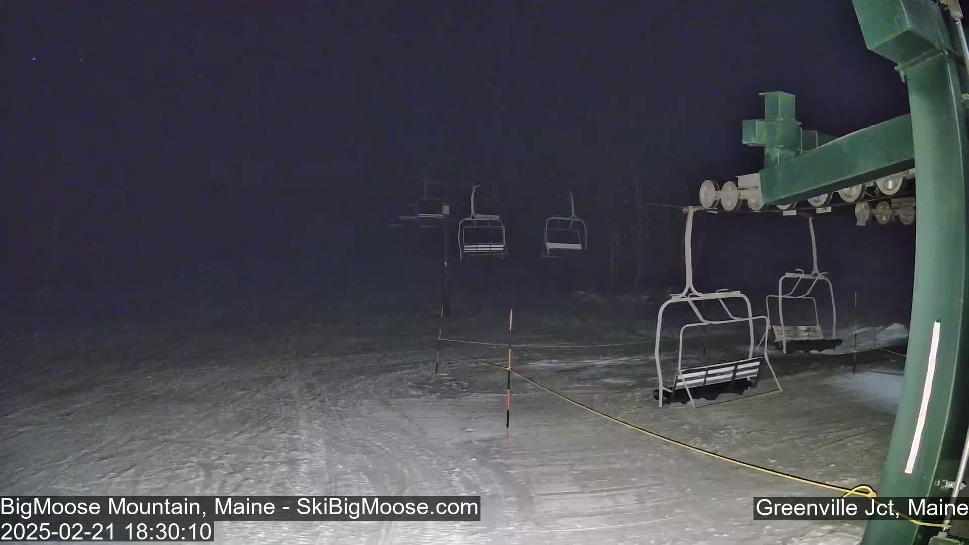 A nighttime, snowy scene shows several empty chairlifts at a ski resort under a dark sky.