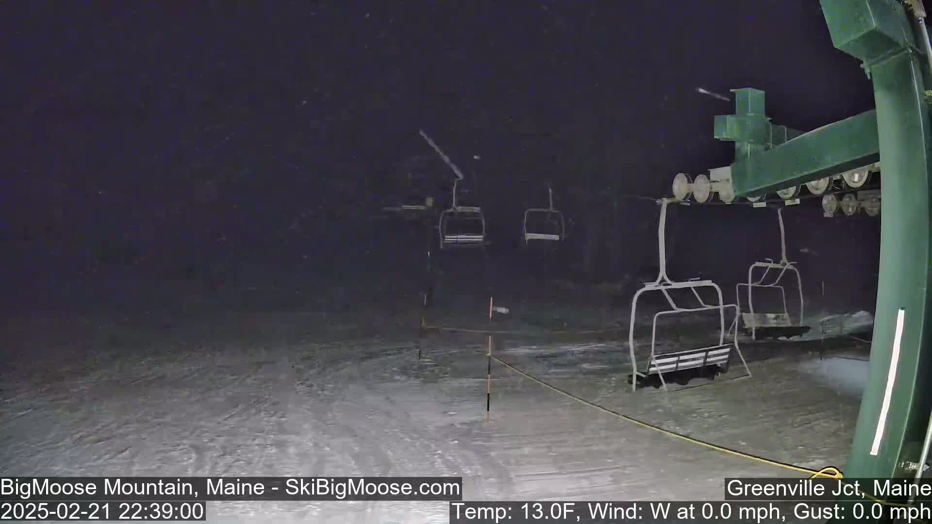 Empty chairlifts sit under a nighttime snowfall on a snow-covered ski slope.