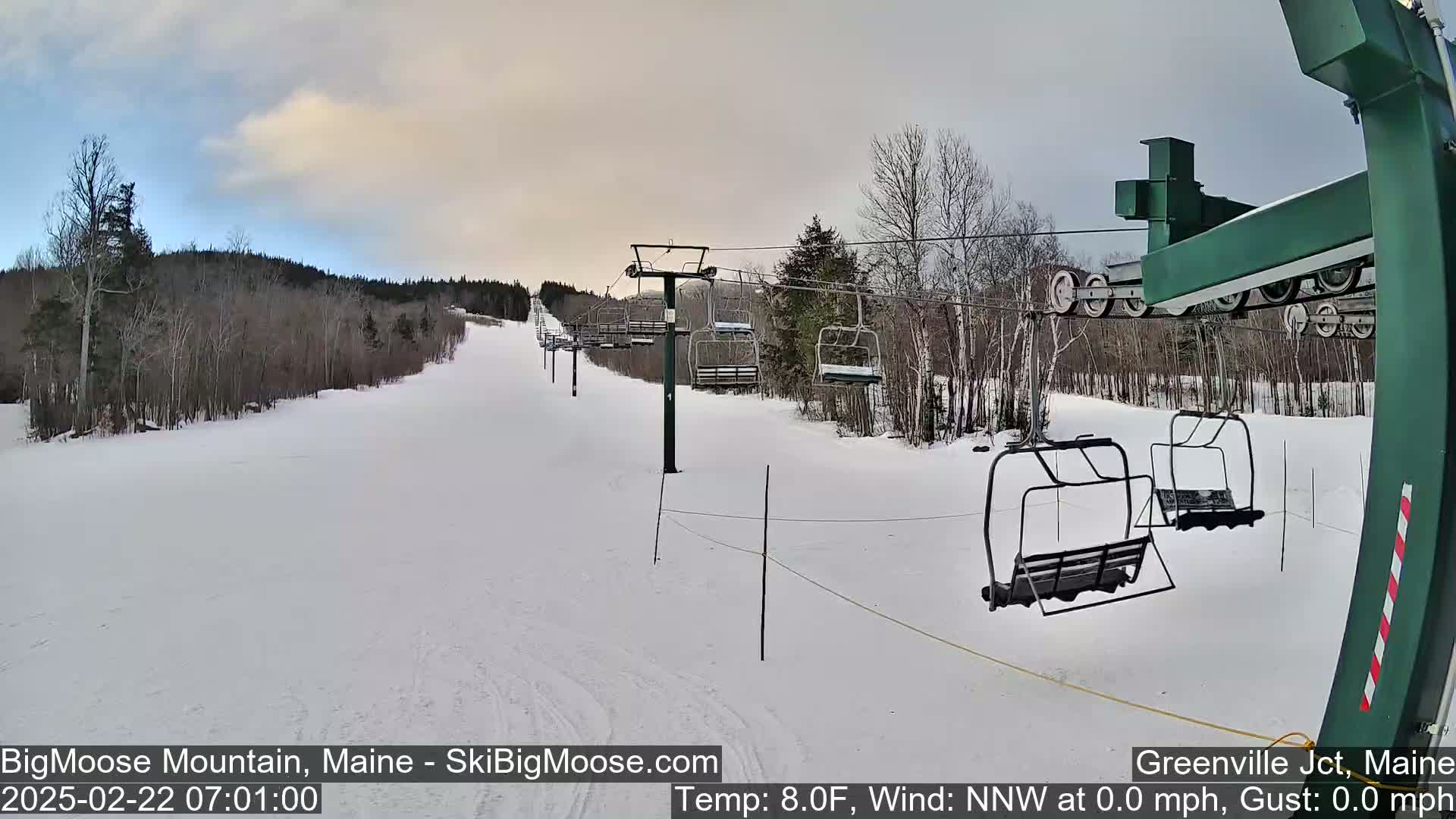 A ski lift with empty chairs ascends a snow-covered slope under an overcast sky.