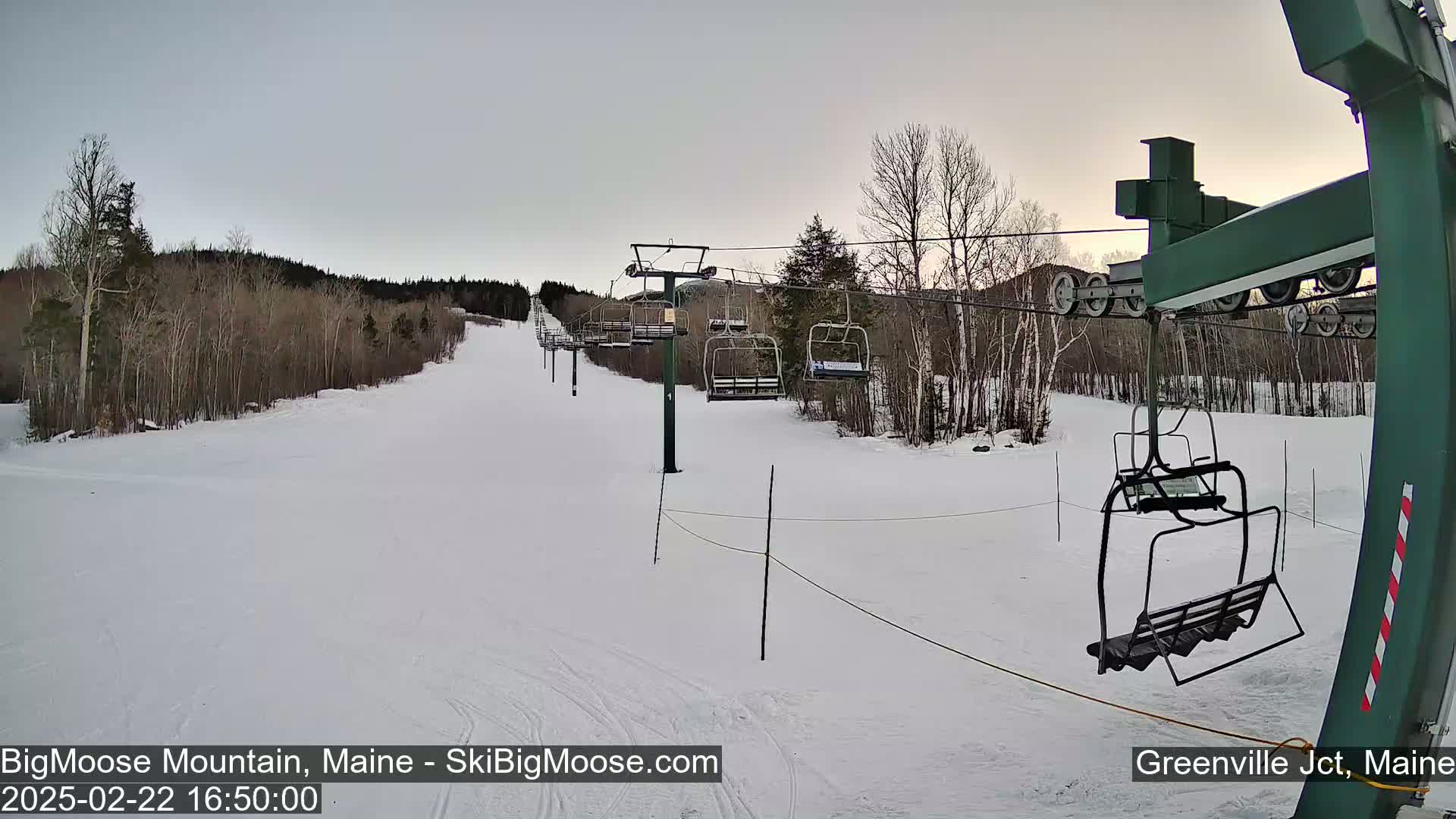 A mostly empty ski lift ascends a snow-covered hill under an overcast sky.
