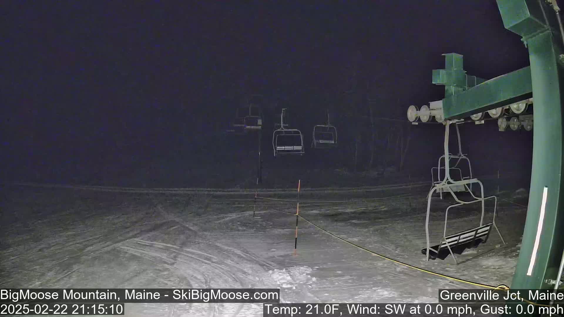 A nighttime view of a snow-covered ski lift with several empty chairlifts under dark, snowy conditions.