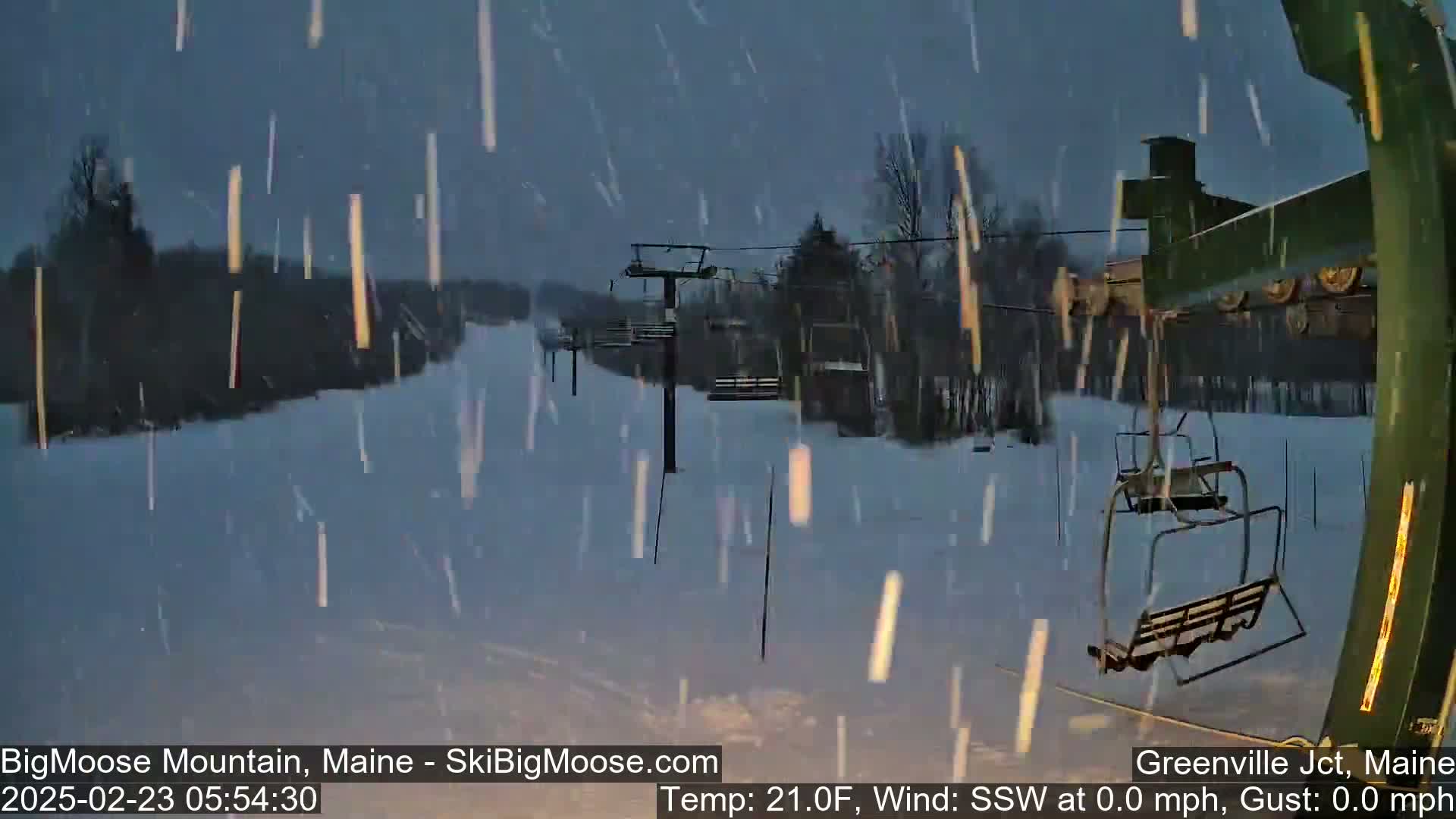 A snow-covered ski lift and slope are visible through falling snow under a dark sky.