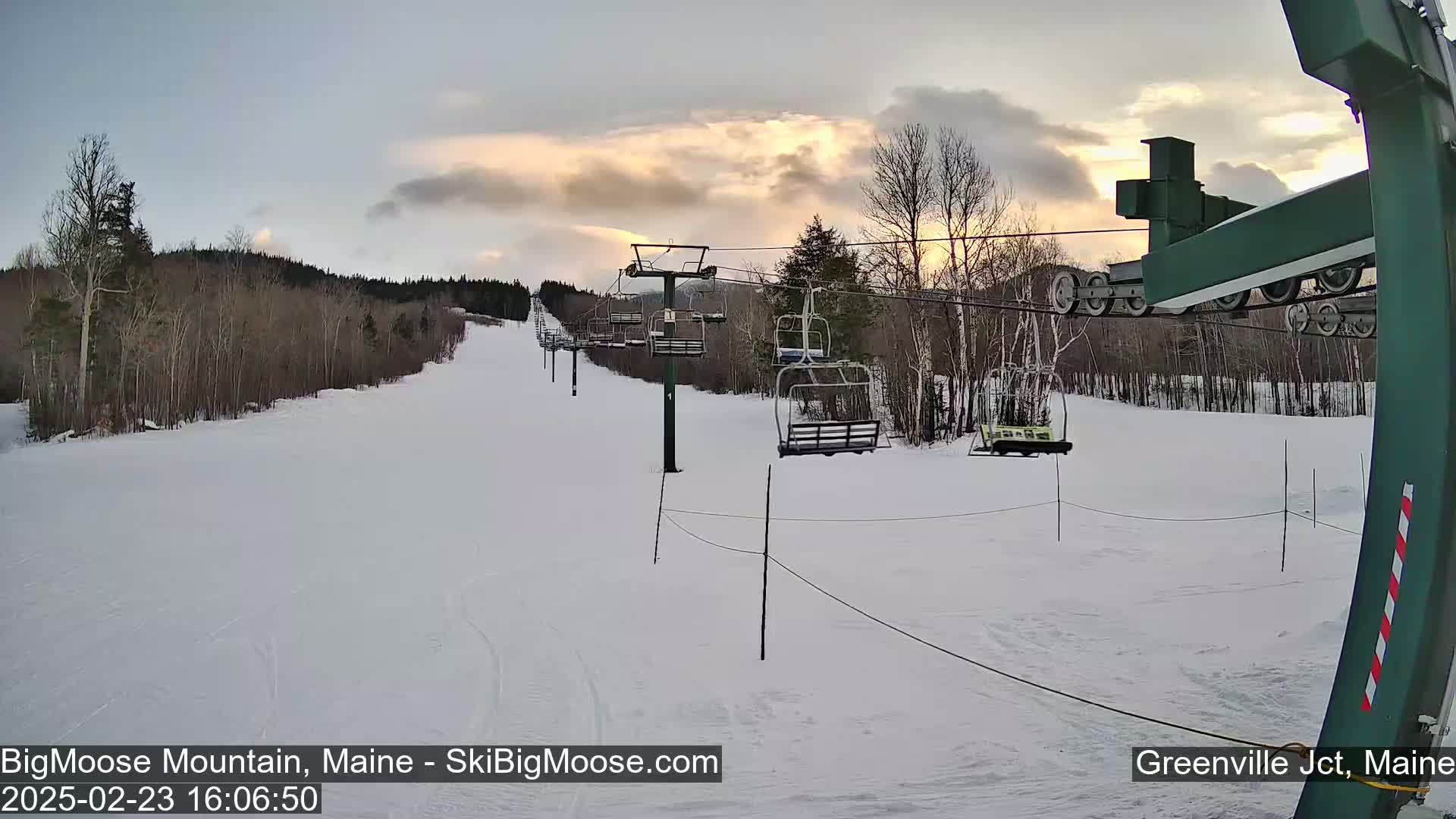 A ski lift ascends a snow-covered slope under a partly cloudy sunset sky.