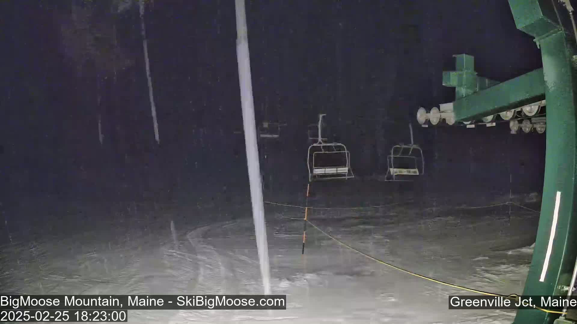 Empty ski lift chairs sit under heavy rain at night.