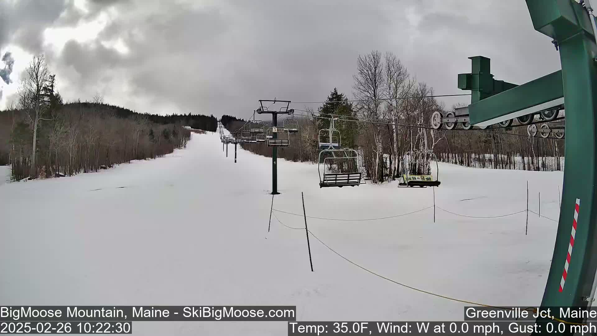 A snow-covered ski slope with a chairlift and trees under an overcast sky.