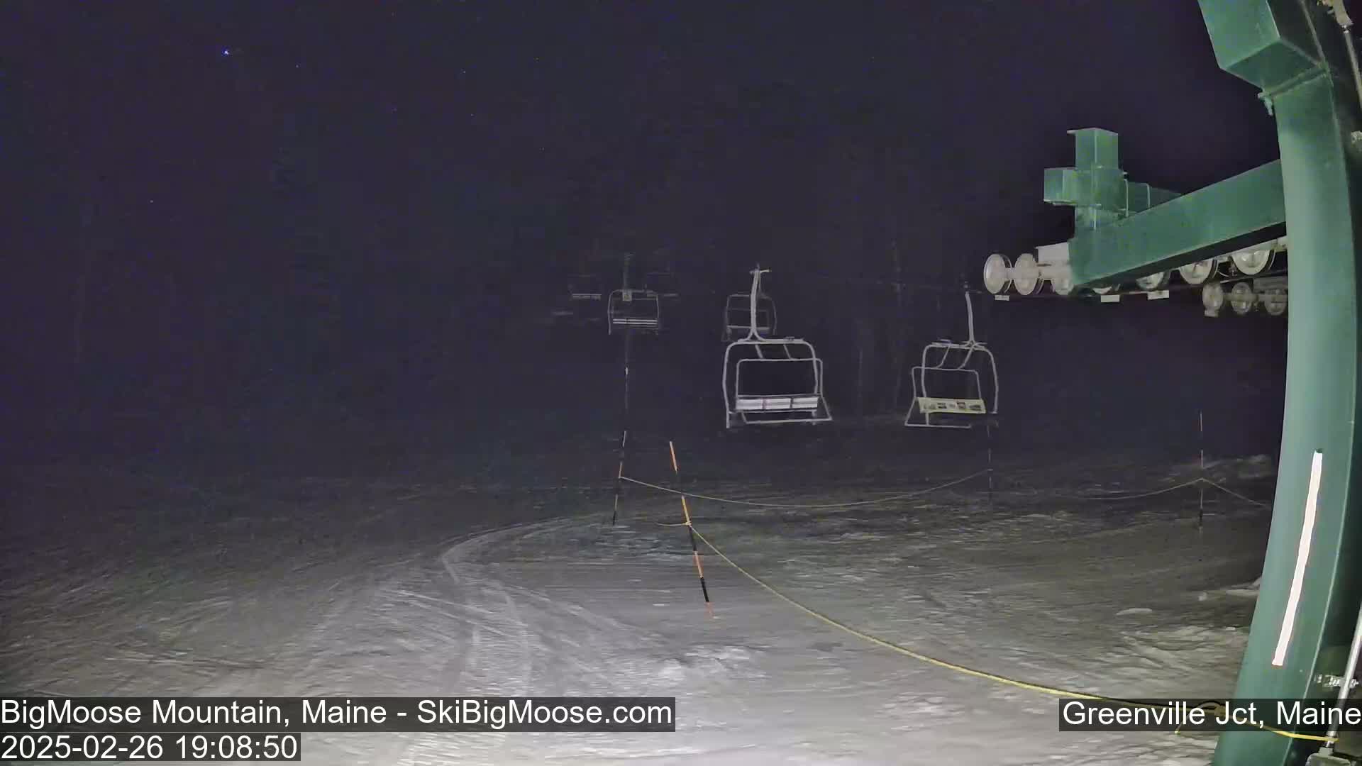 Under a dark, starlit night sky, several empty chairlifts stand on a snow-covered ski slope.