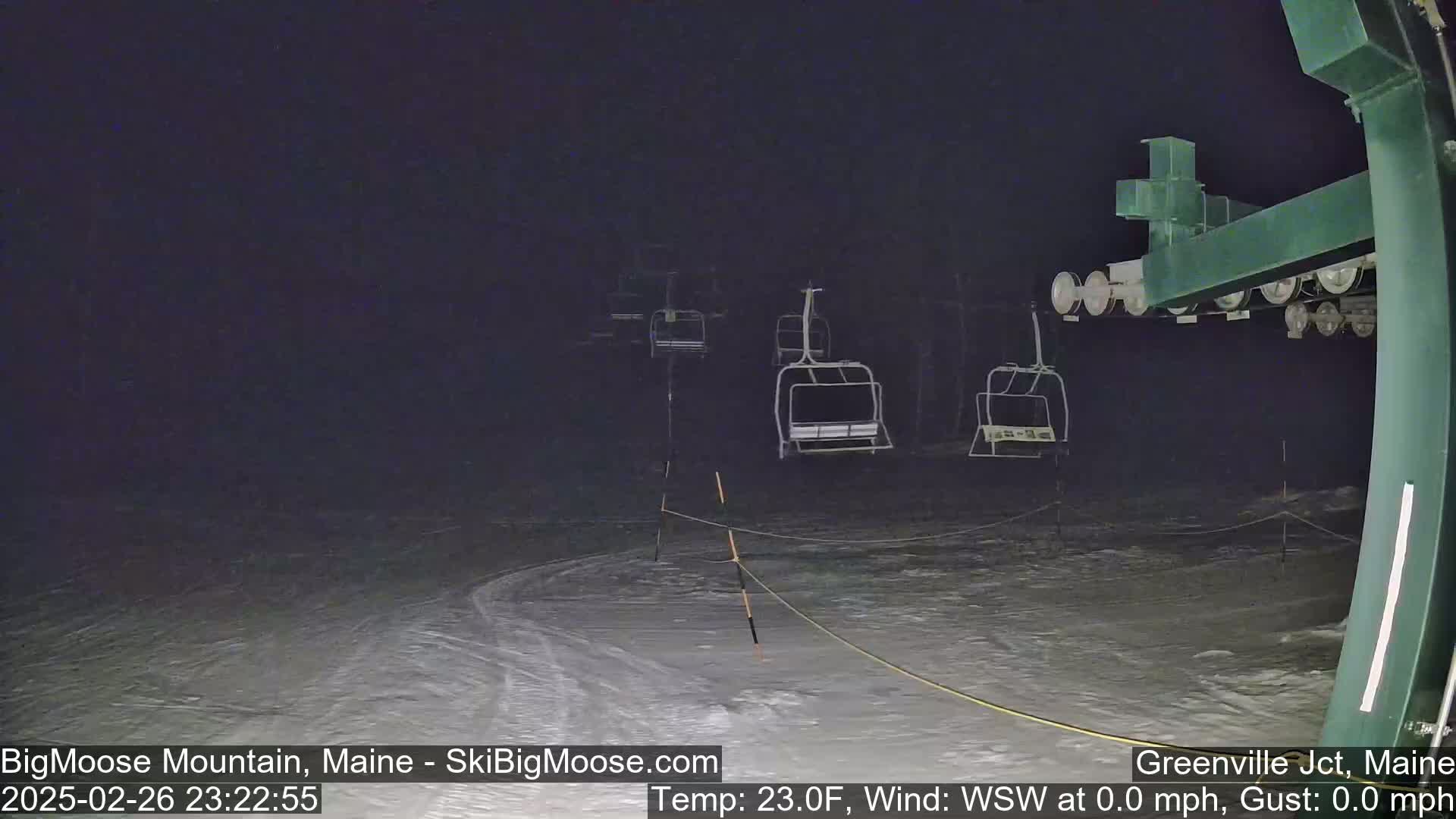 Empty ski lifts stand under a dark, nighttime sky on a snow-covered slope.