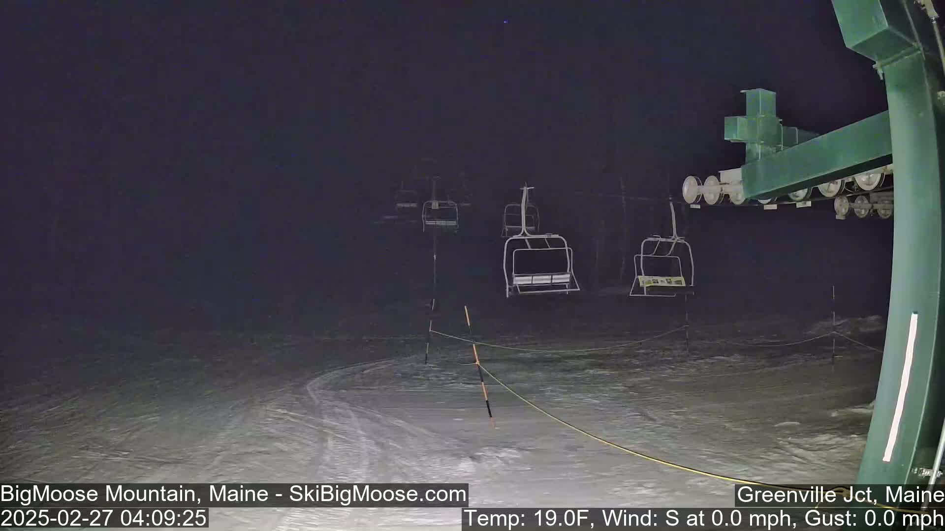 A nighttime view of a snow-covered ski slope with several empty chairlifts under a dark, clear sky.
