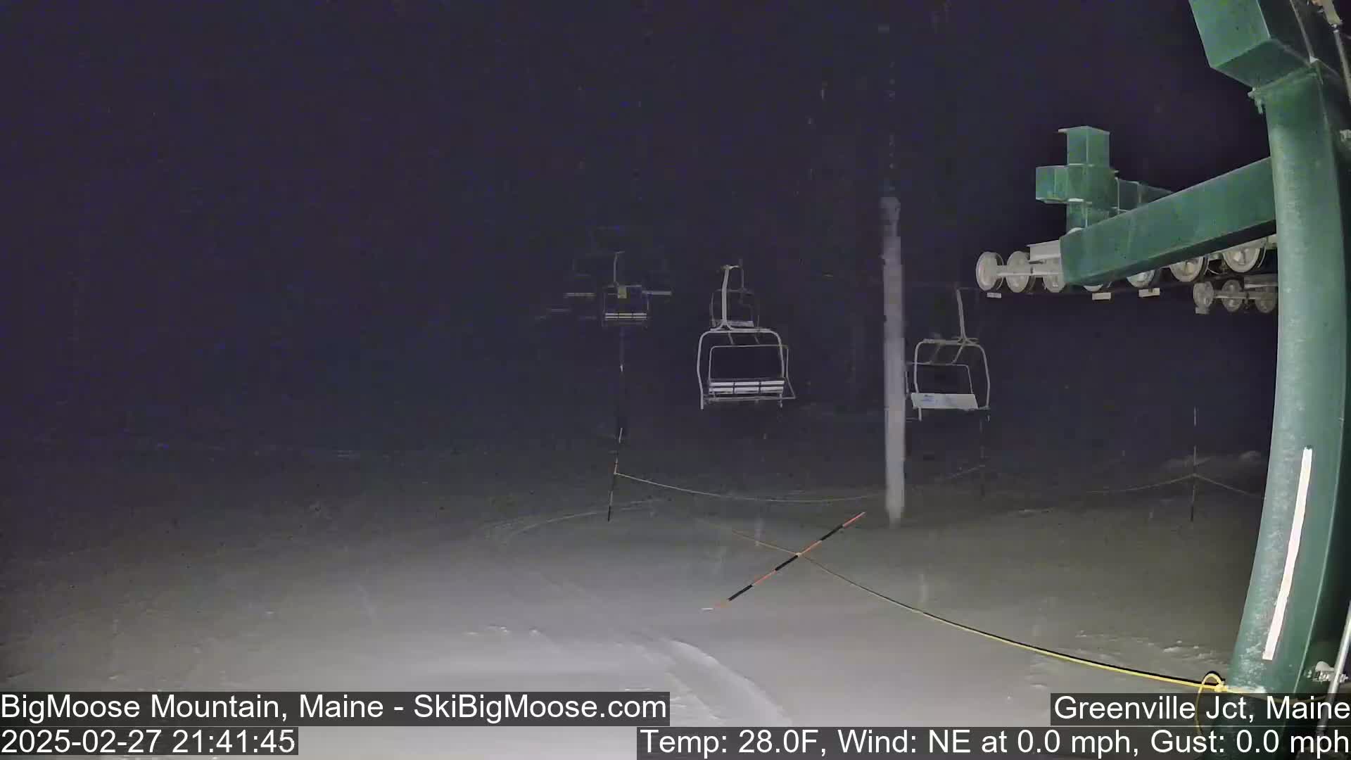A nighttime view of a ski lift with empty chairs under snowy conditions, at 28 degrees Fahrenheit with a calm wind.