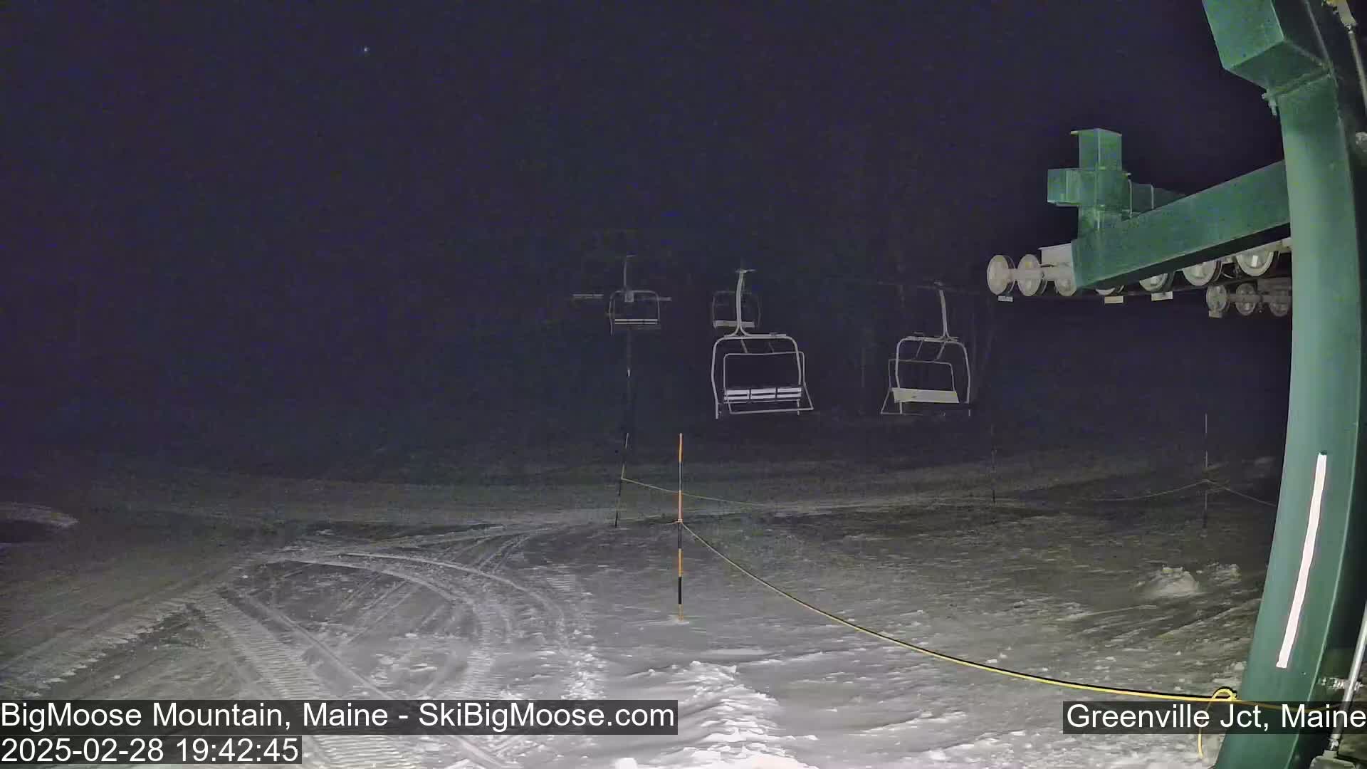At night, under a dark sky, a ski lift with empty chairs stands on a snow-covered slope.