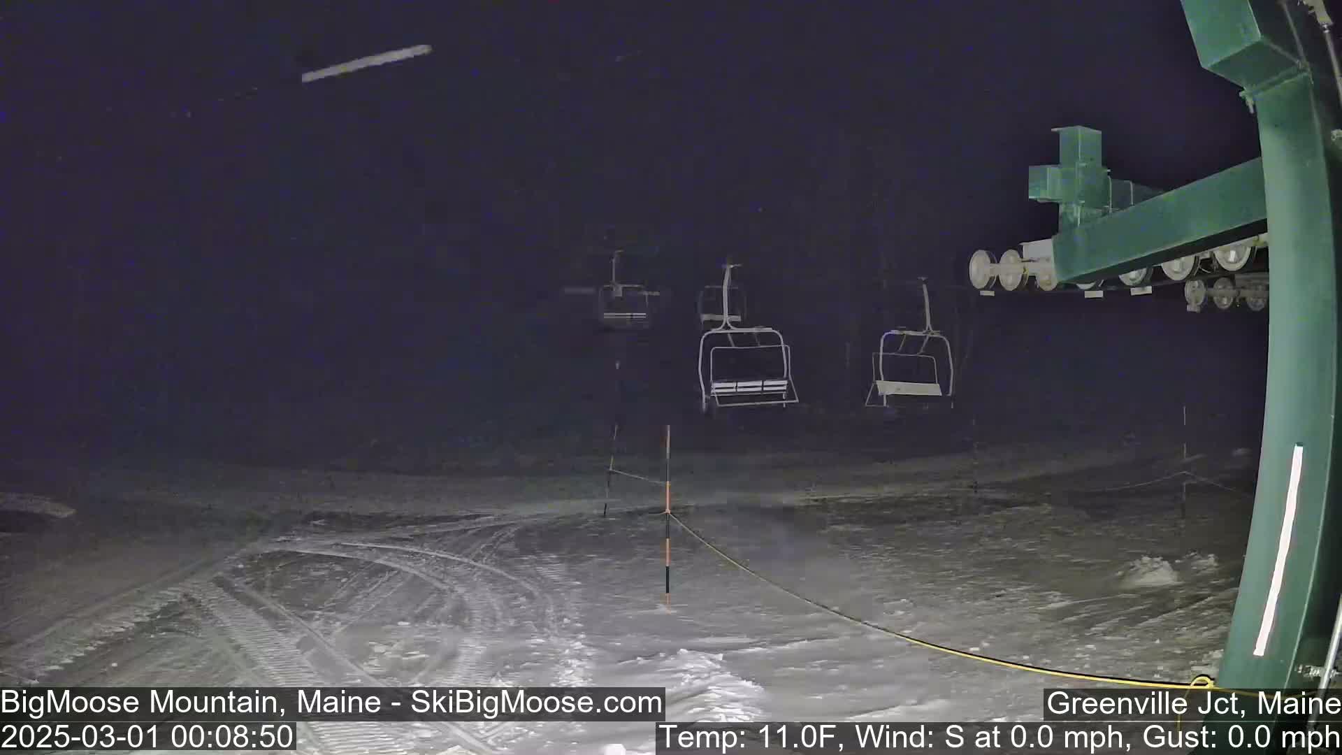 At night, under a dark sky, several empty chairlifts sit on a snow-covered ski slope with calm, windless conditions and a temperature of 11 degrees Fahrenheit.