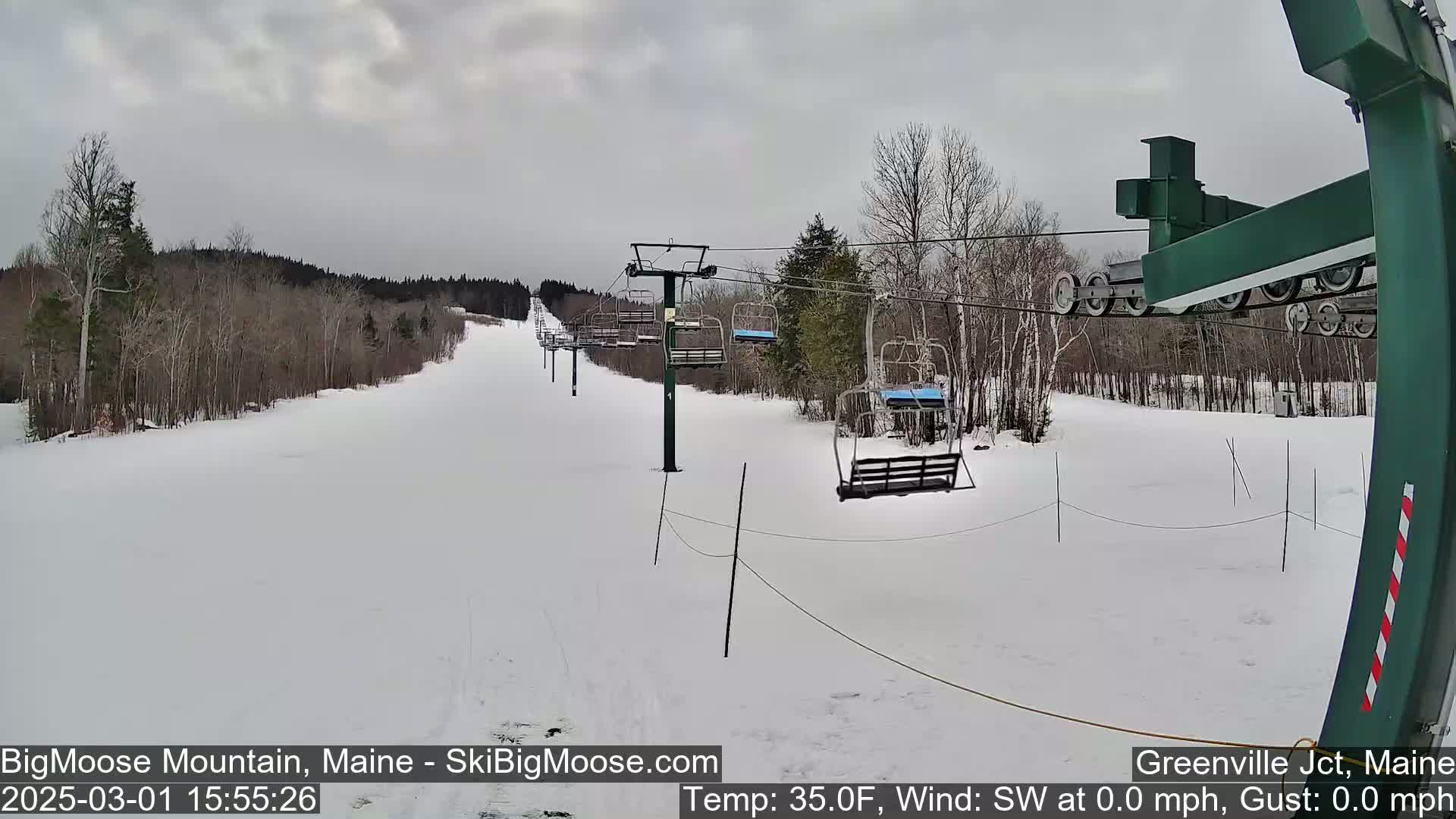 A snow-covered ski slope with a chairlift and trees under a cloudy sky.