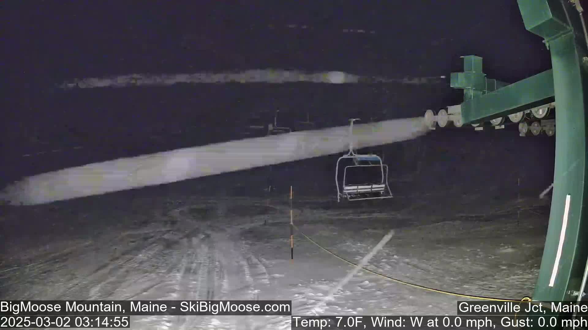 A chairlift sits on a snowy ski slope at night under light snowfall.
