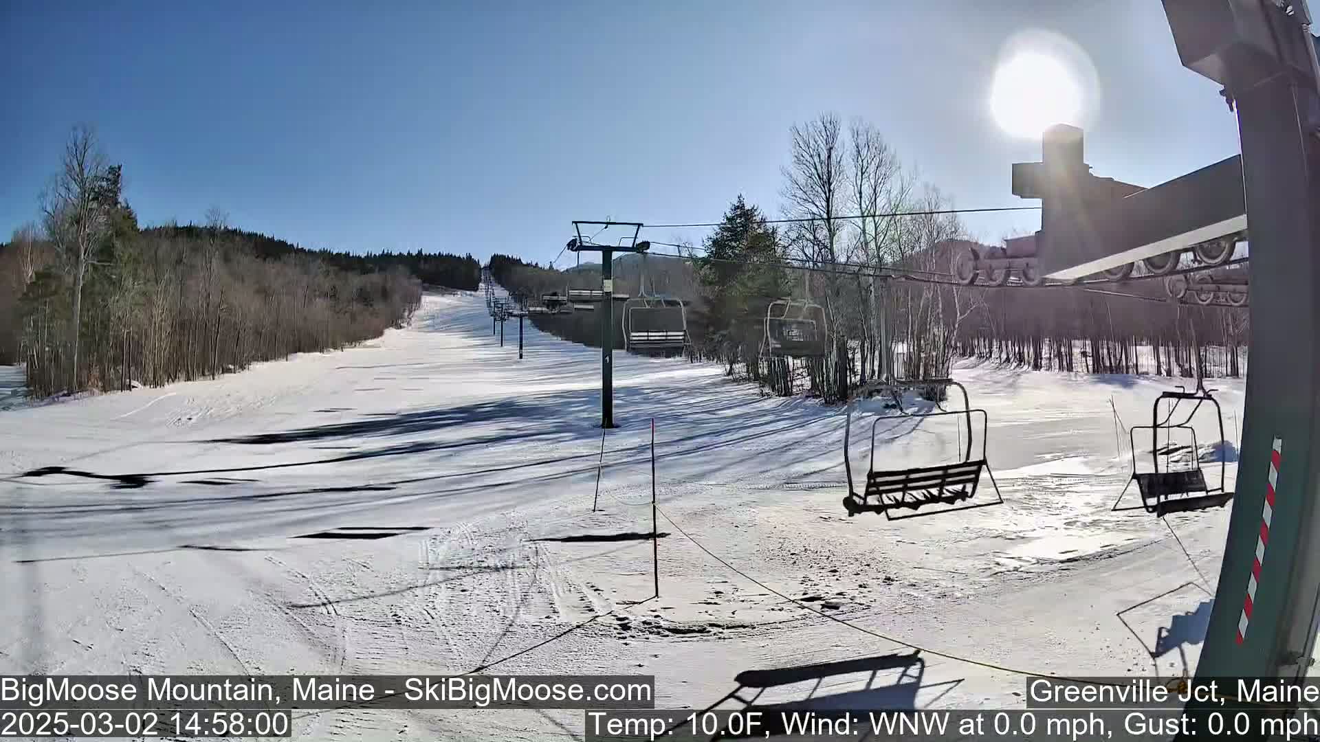 A sunny, snow-covered ski slope with several empty chairlifts under a clear blue sky.