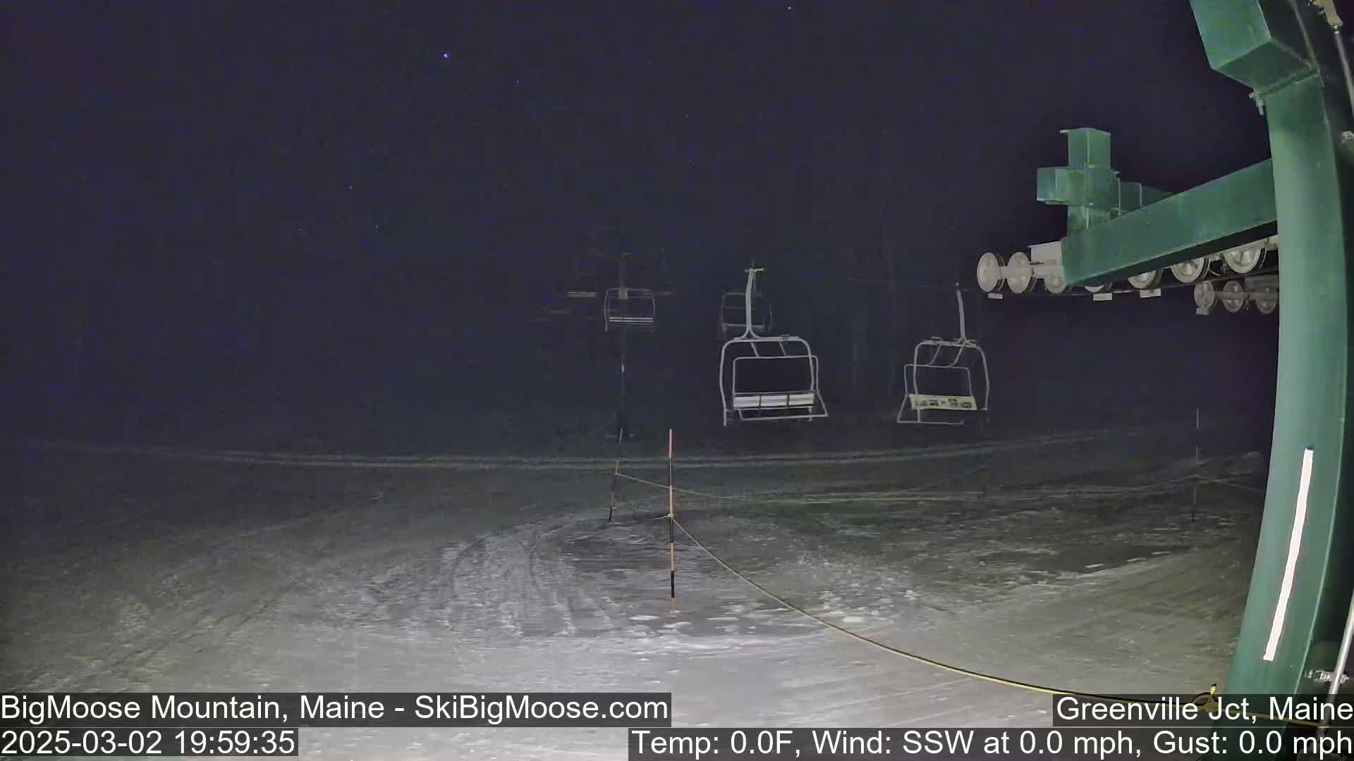 Under a clear, starry night sky, several empty chairlifts sit on a snow-covered ski slope.