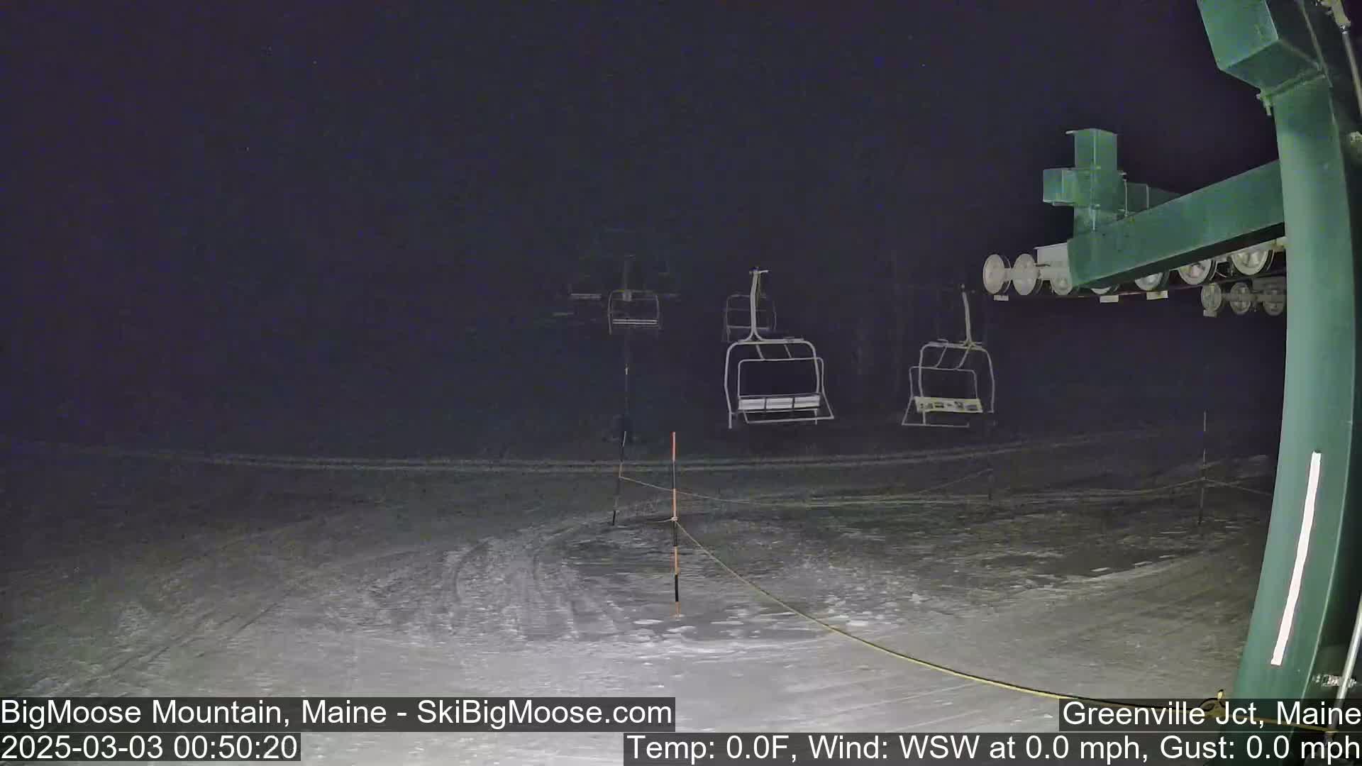 A nighttime view of a snow-covered ski slope with several empty chairlifts under a dark sky.