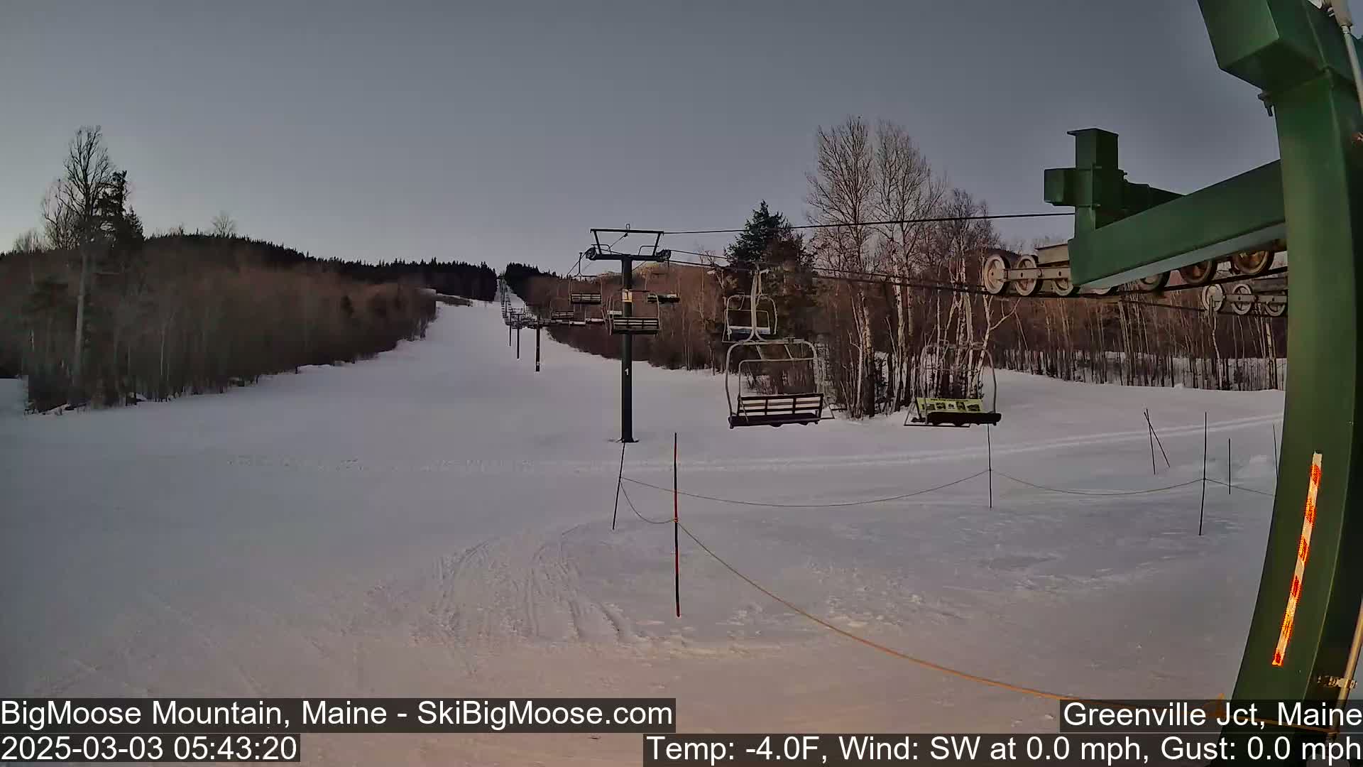 A mostly empty ski lift ascends a snow-covered hill under a twilight sky.