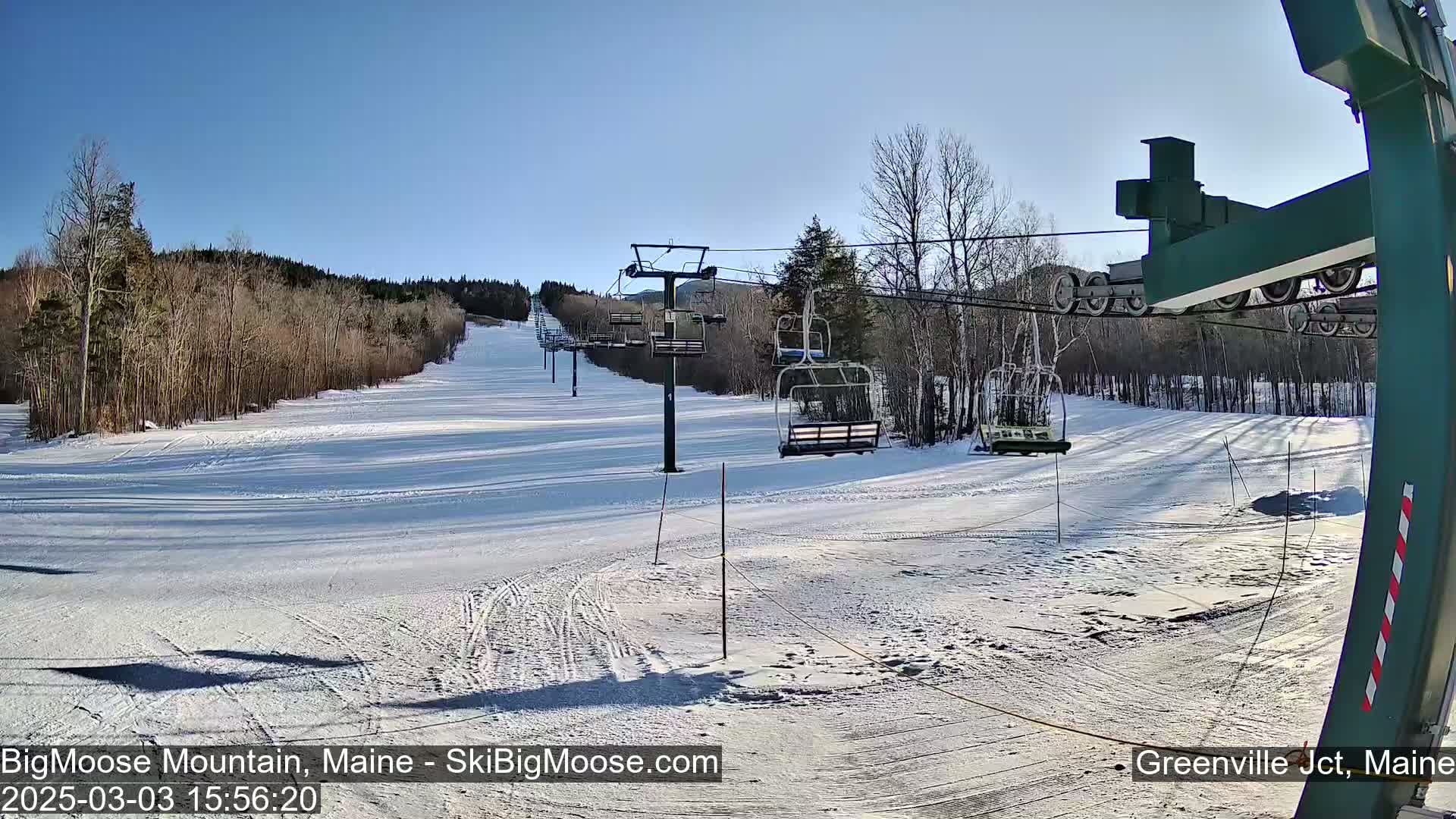 A snow-covered ski slope with a chairlift and bare trees under a clear blue sky.