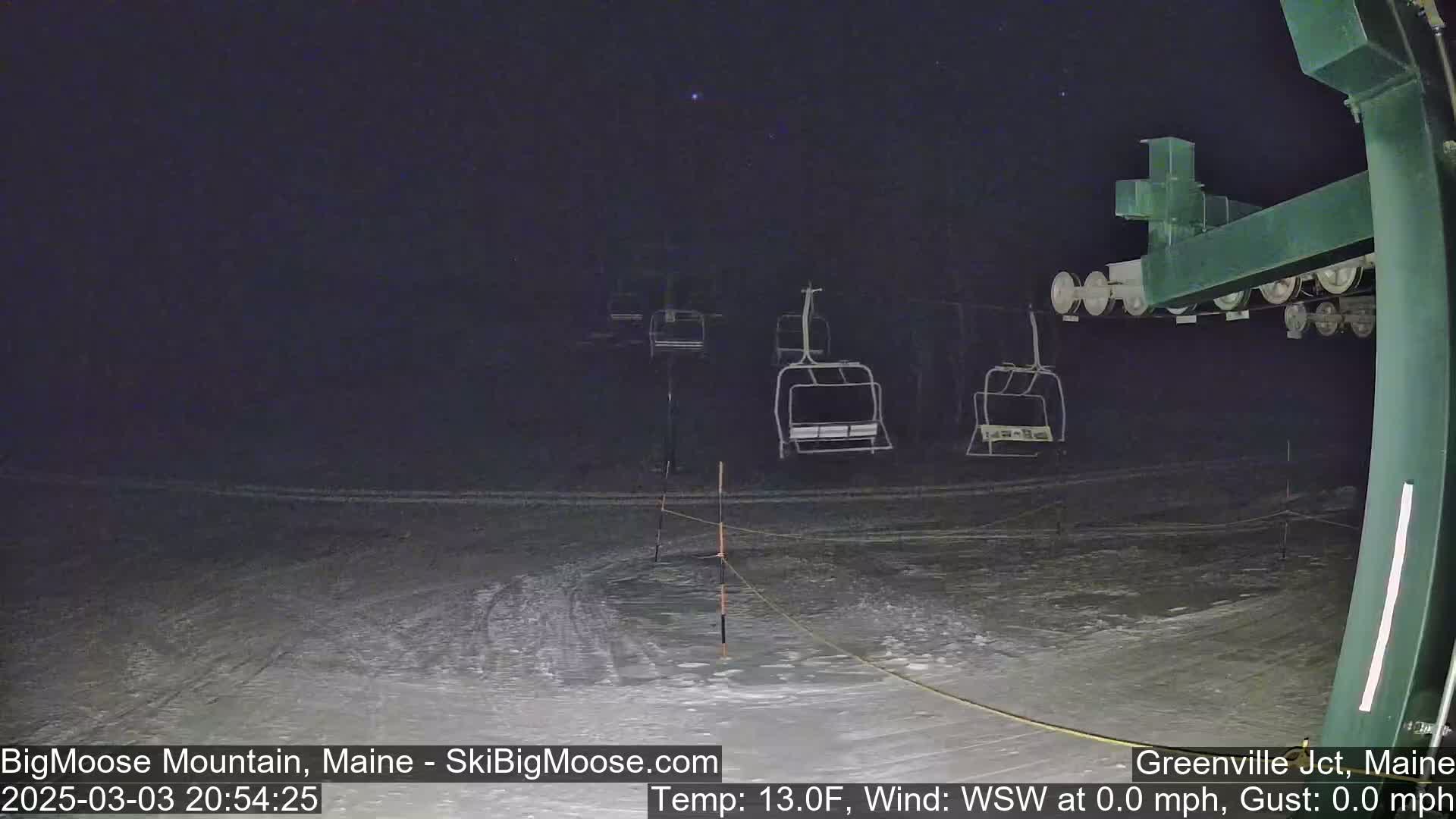 A nighttime view of a snow-covered ski lift with several empty chairs under a clear, starry sky.