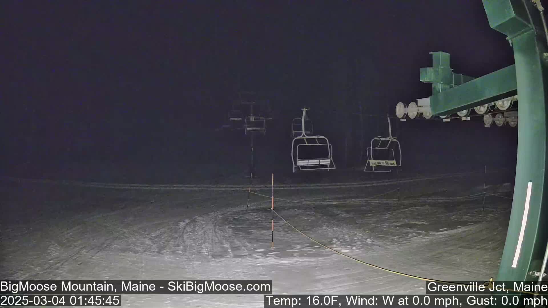 A nighttime view of a snow-covered ski lift with empty chairs under a dark sky.