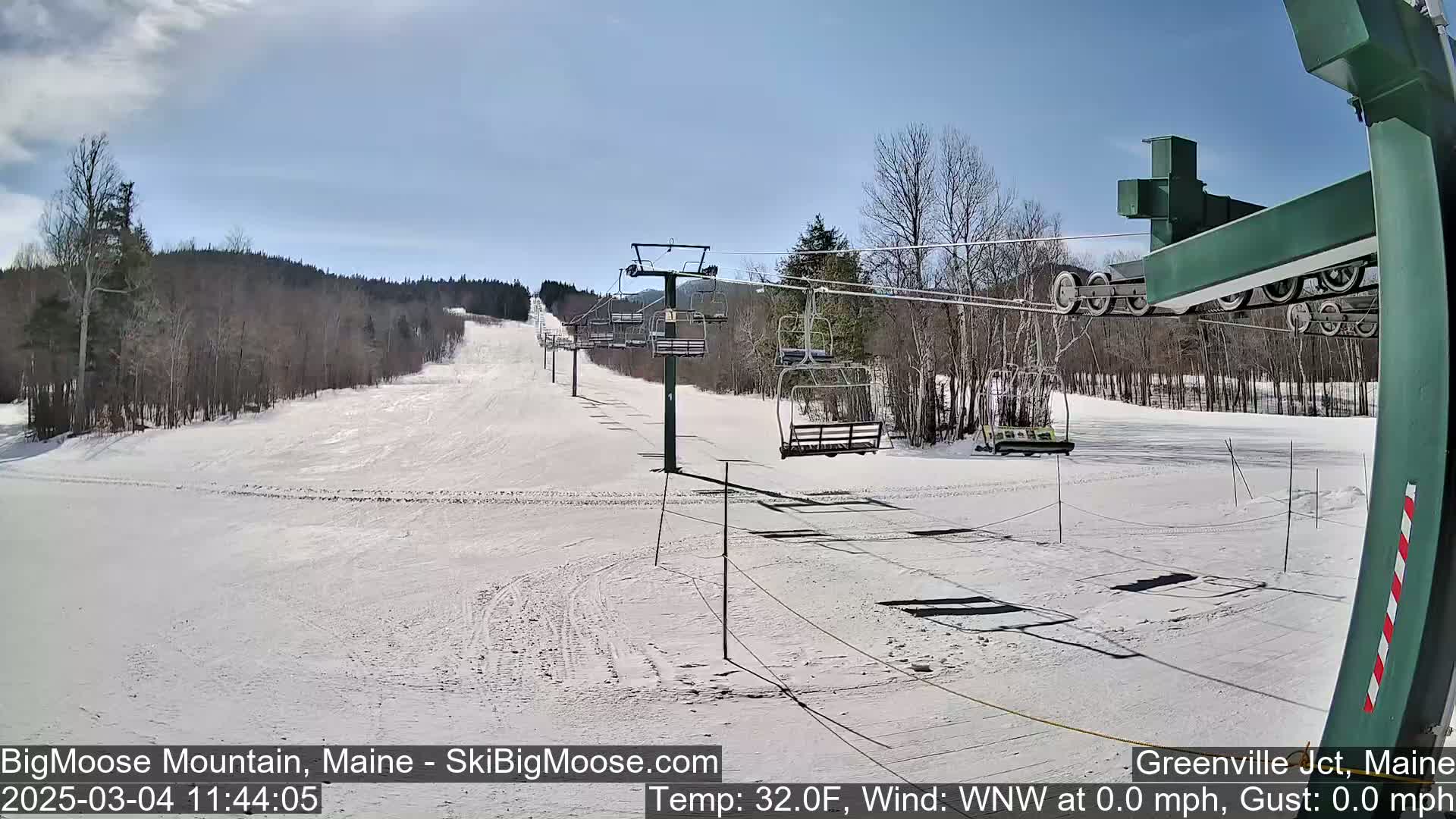 A snow-covered ski slope with a chairlift and surrounding trees under a clear, bright sky.