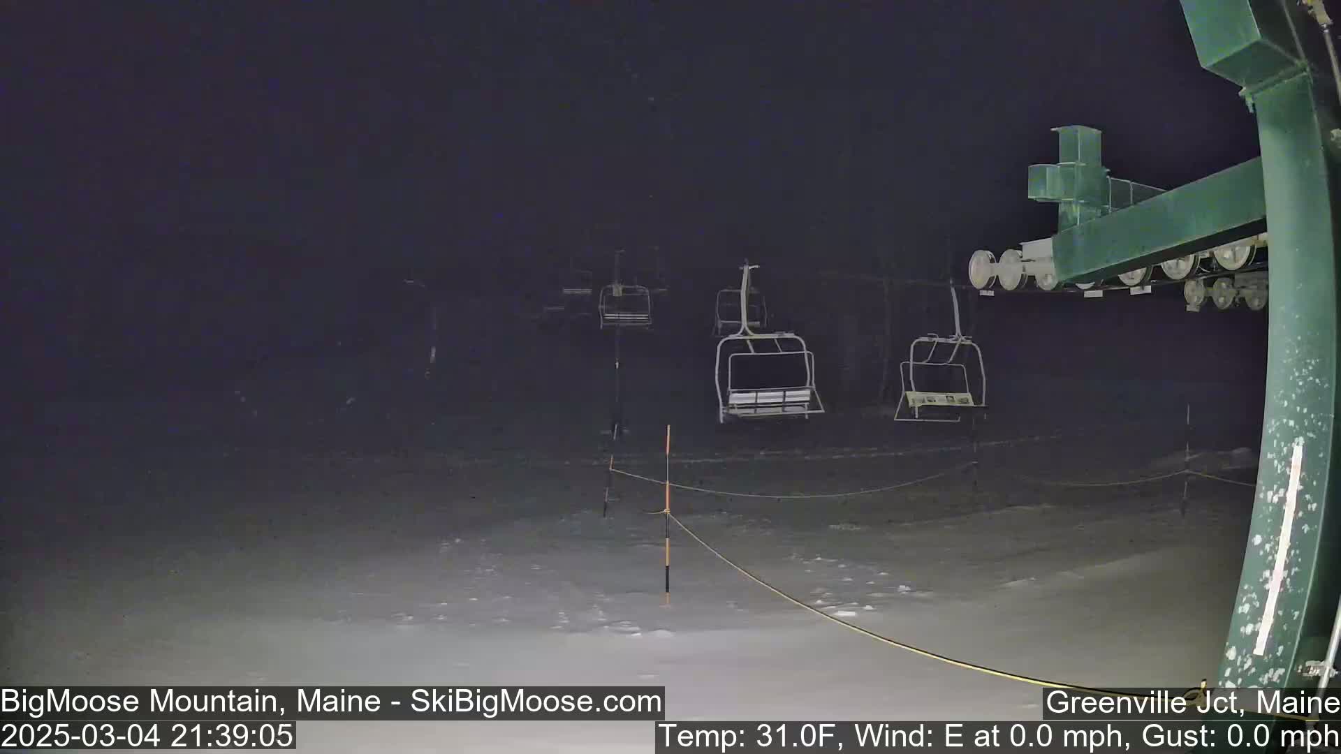 A nighttime view of a snow-covered ski lift with several empty chairlifts, under calm conditions.