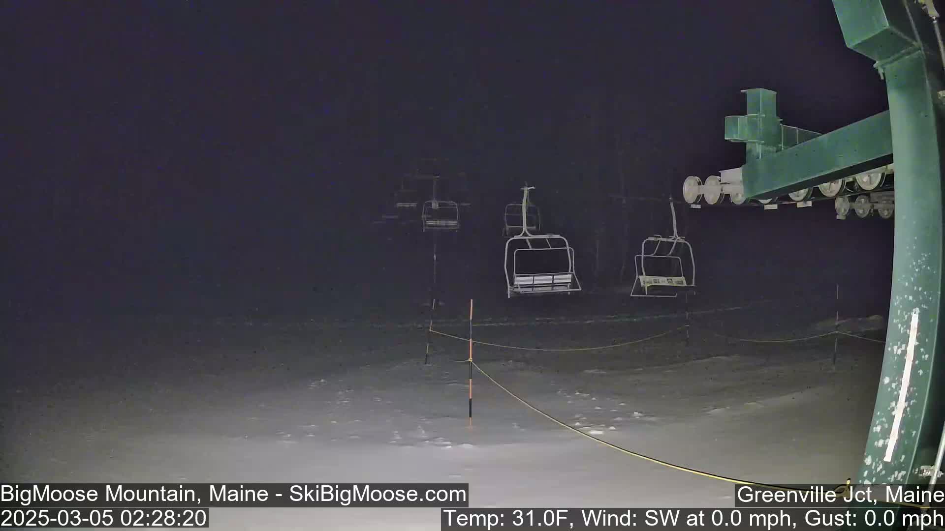A nighttime view of a snow-covered ski lift with several empty chairs under a dark sky.