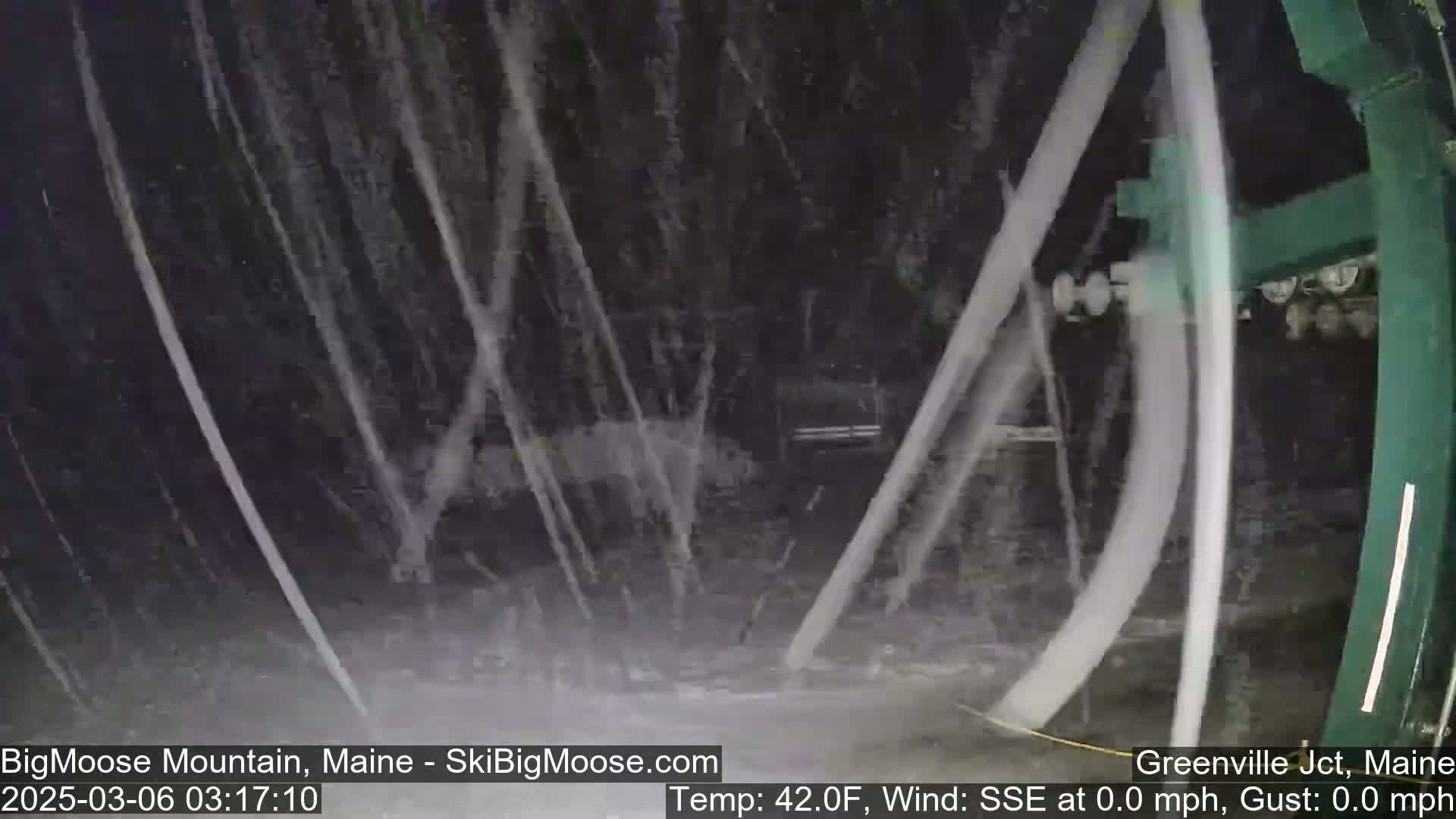 Heavy rain falls on a dark, blurry scene partially obscured by a moving chairlift.
