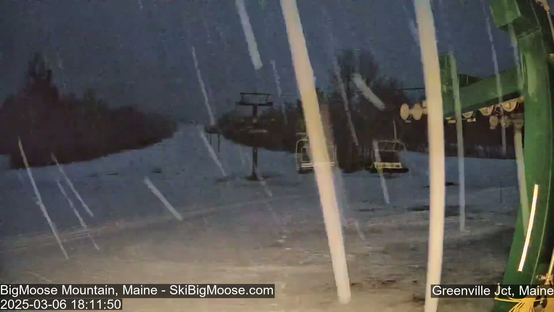 A snowy scene at a ski resort shows a chairlift and snow falling heavily in the twilight.