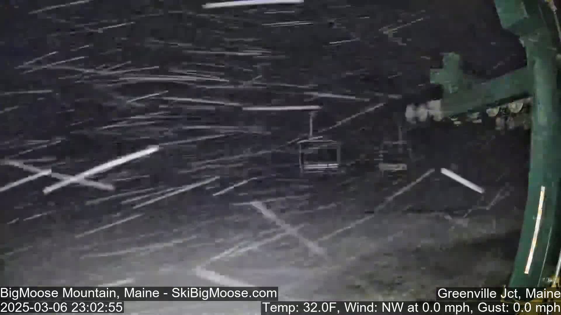 Heavy snow falls at night, obscuring a ski lift and the surrounding area.