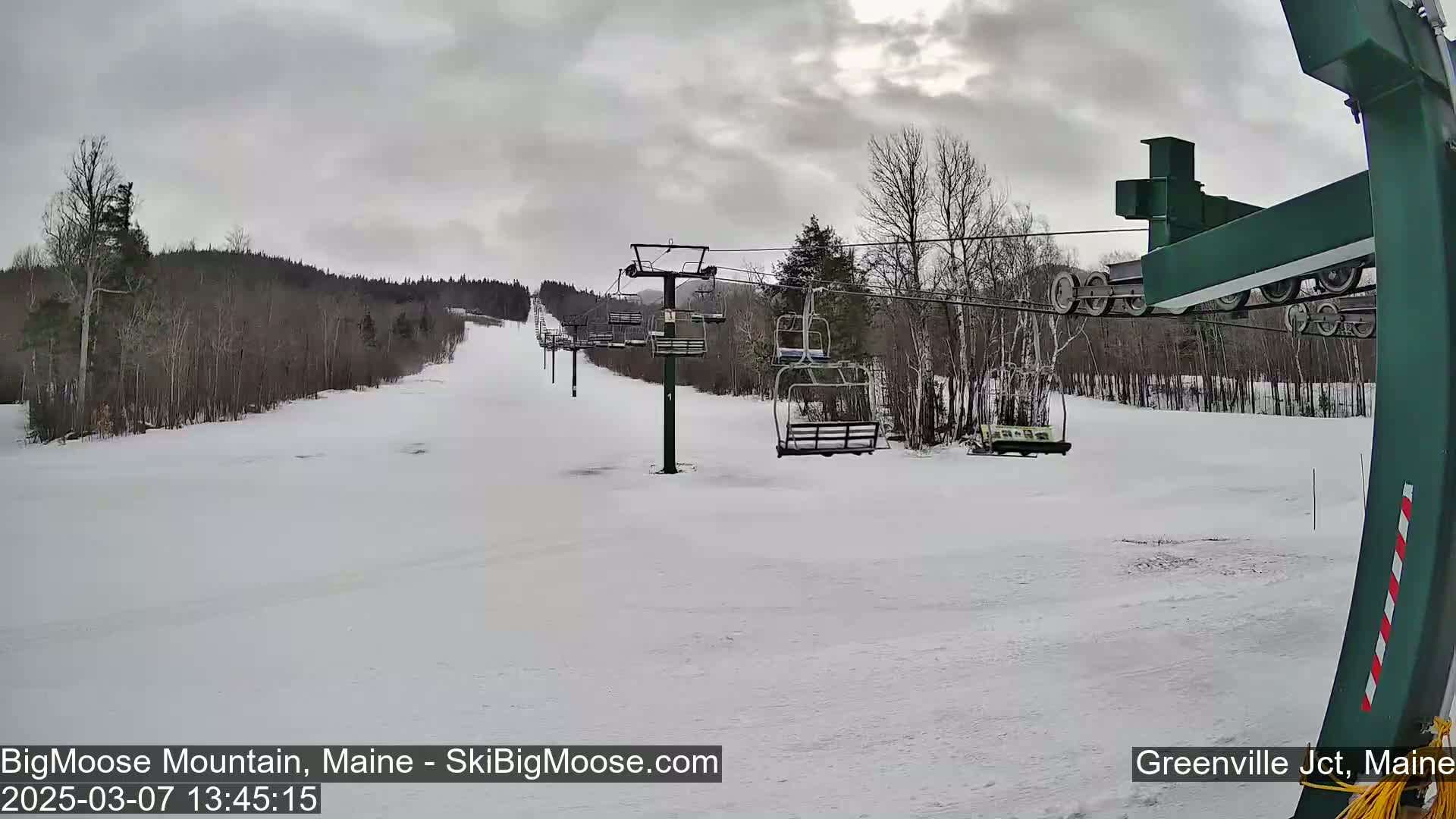 A snow-covered ski slope with a chairlift and bare trees under an overcast sky.