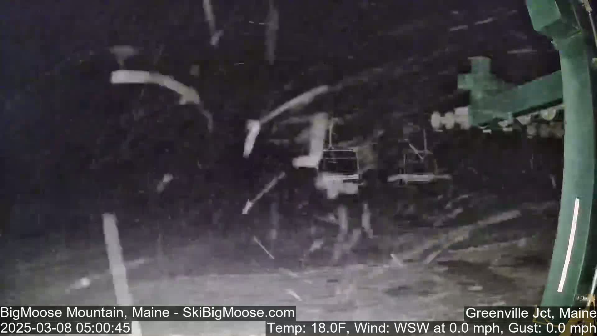 Snow falls heavily around a dark-colored ski lift in the nighttime.