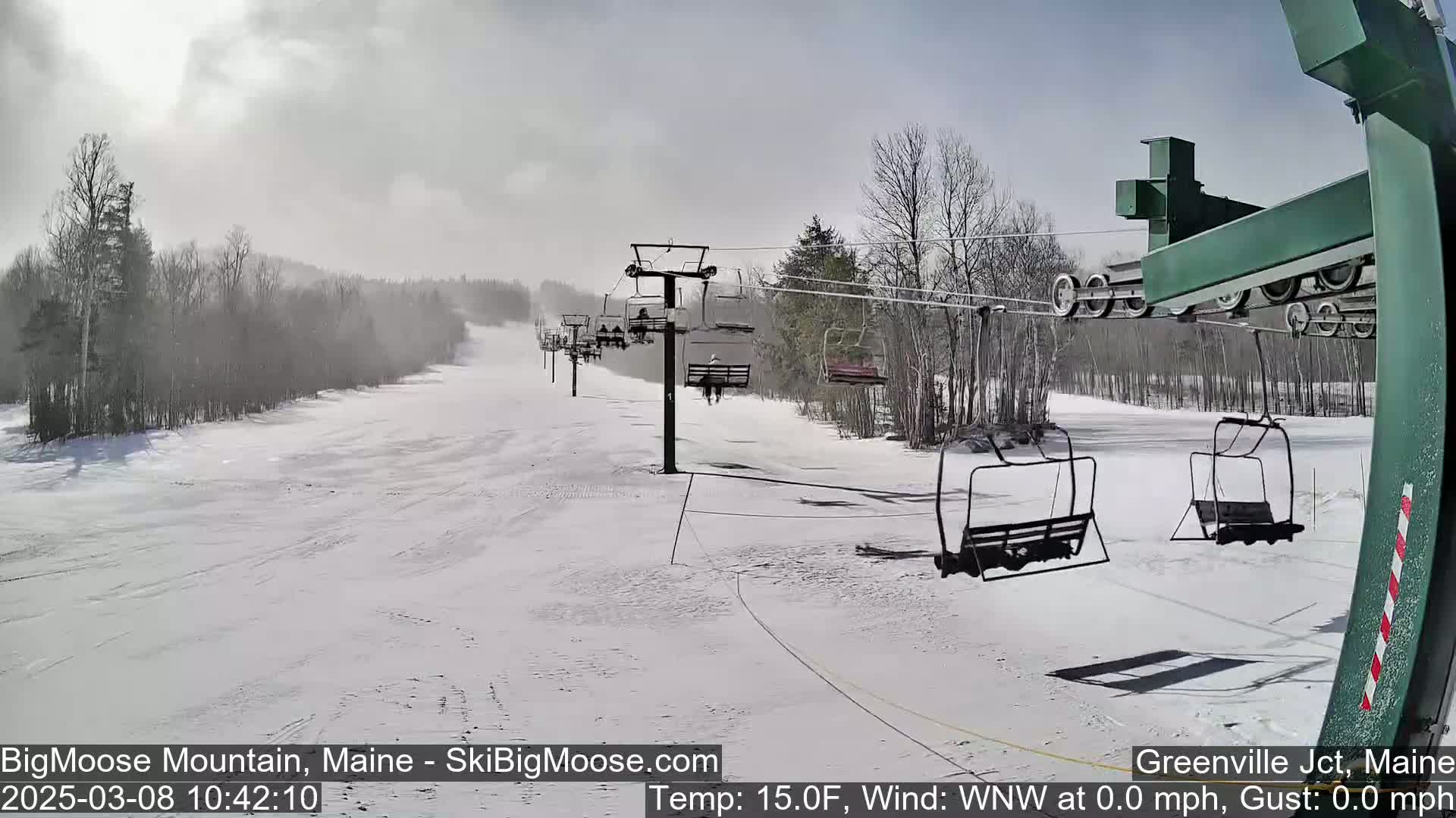 A snow-covered ski slope with a chairlift and several empty chairs, under a hazy sky.