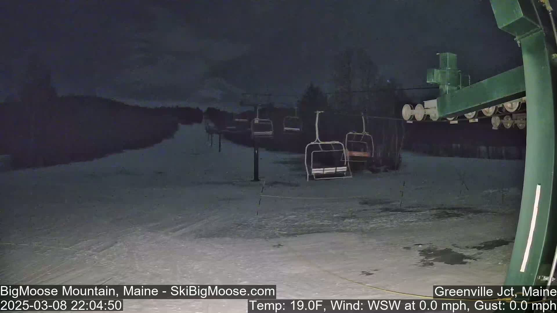A nighttime view of a snow-covered ski slope with several empty chairlifts under a dark, cloudy sky.
