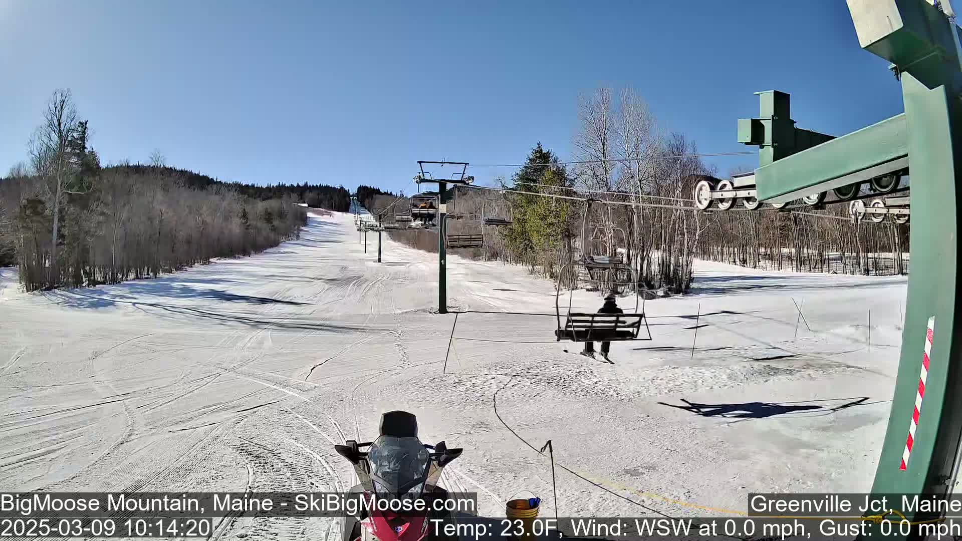 A snow-covered ski slope with a chairlift and skiers on a sunny day.