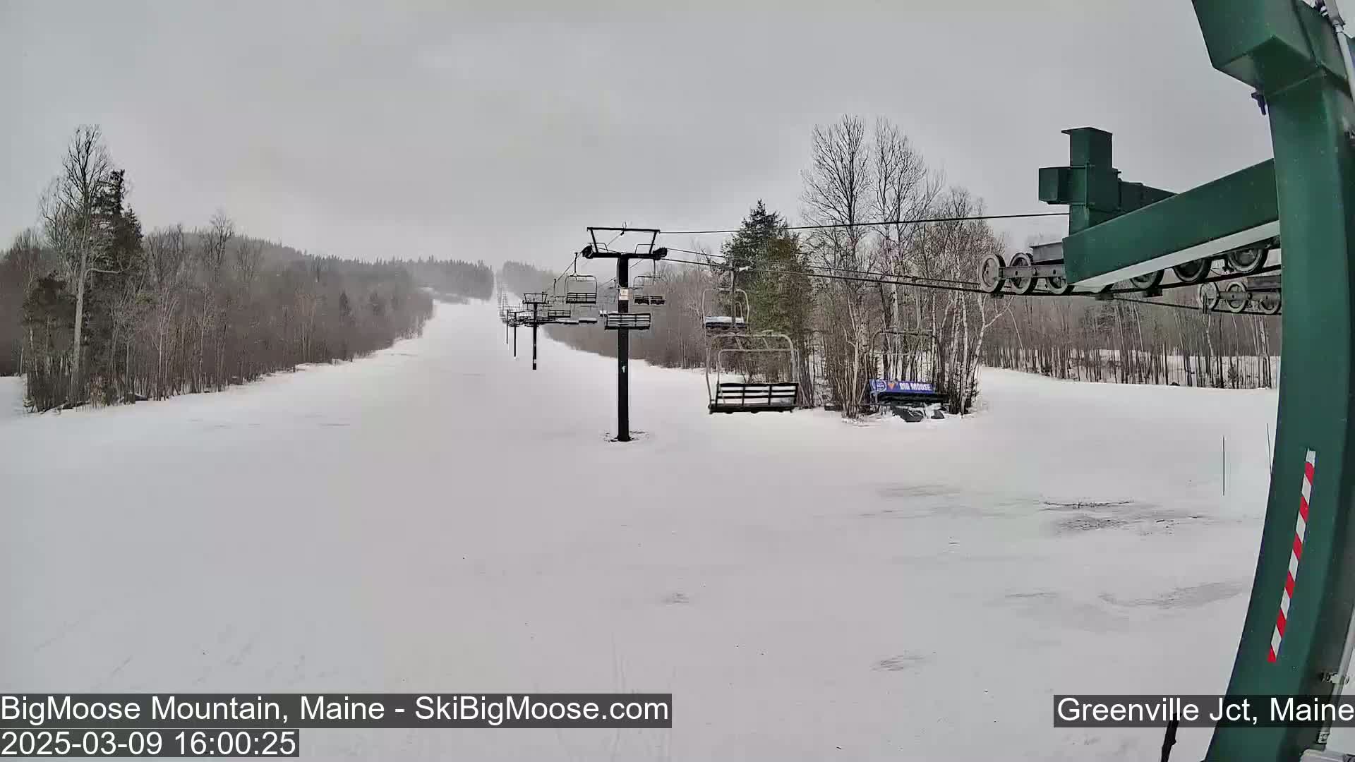A snow-covered ski slope with a chairlift and bare trees under an overcast sky.