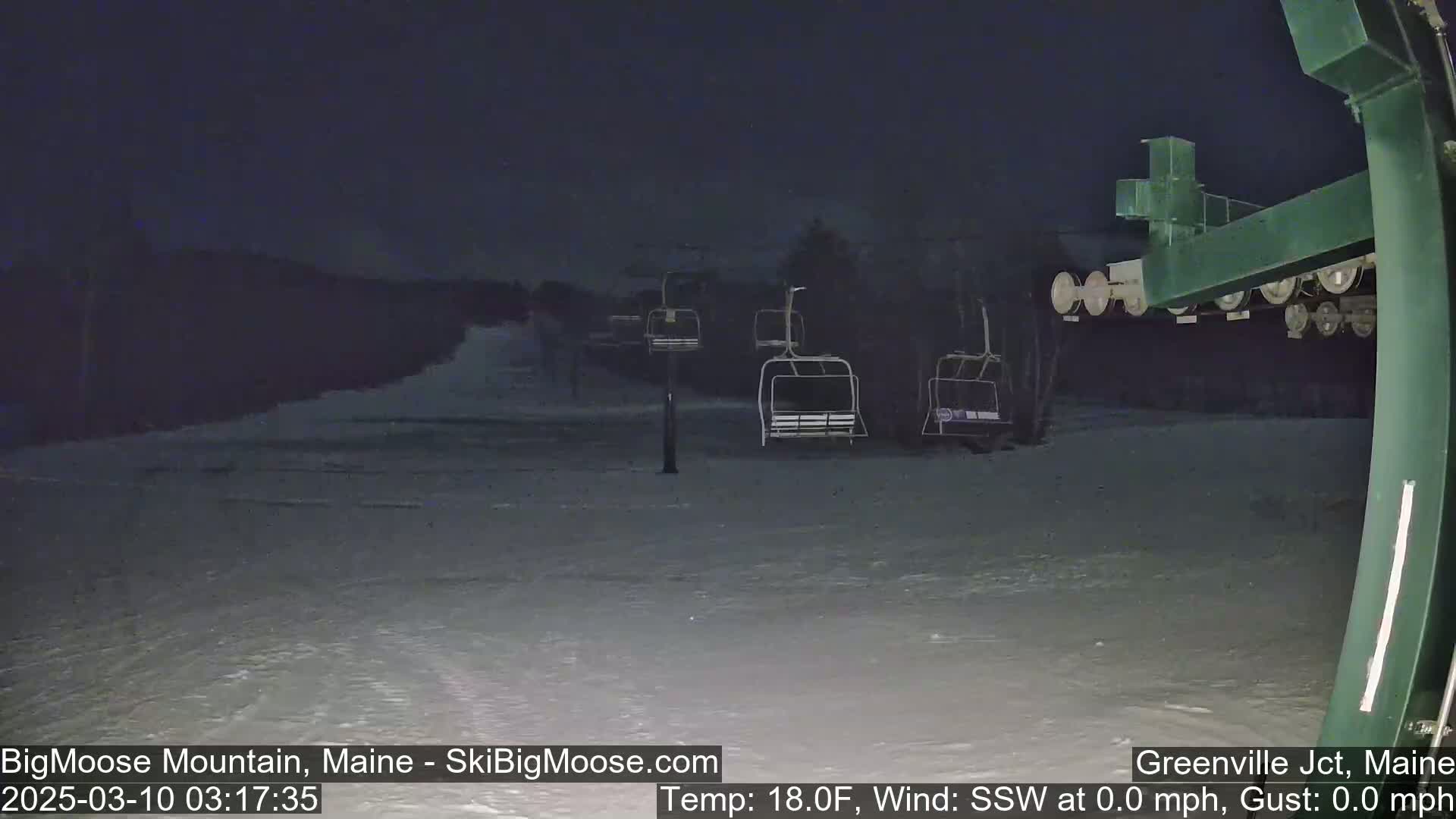 A nighttime view of a snow-covered ski slope with empty chairlifts under a dark sky.