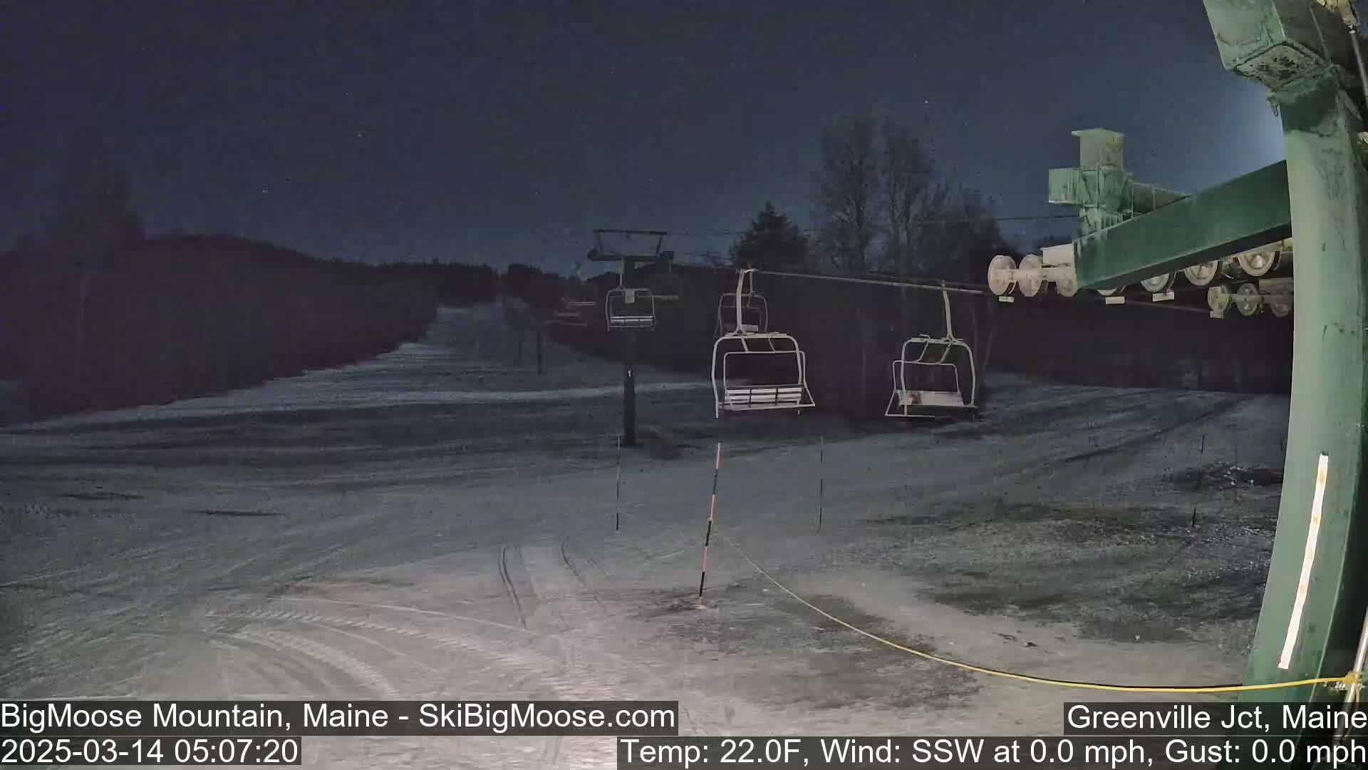 Under a dark night sky, a ski lift with empty chairs stands on a snow-covered slope.