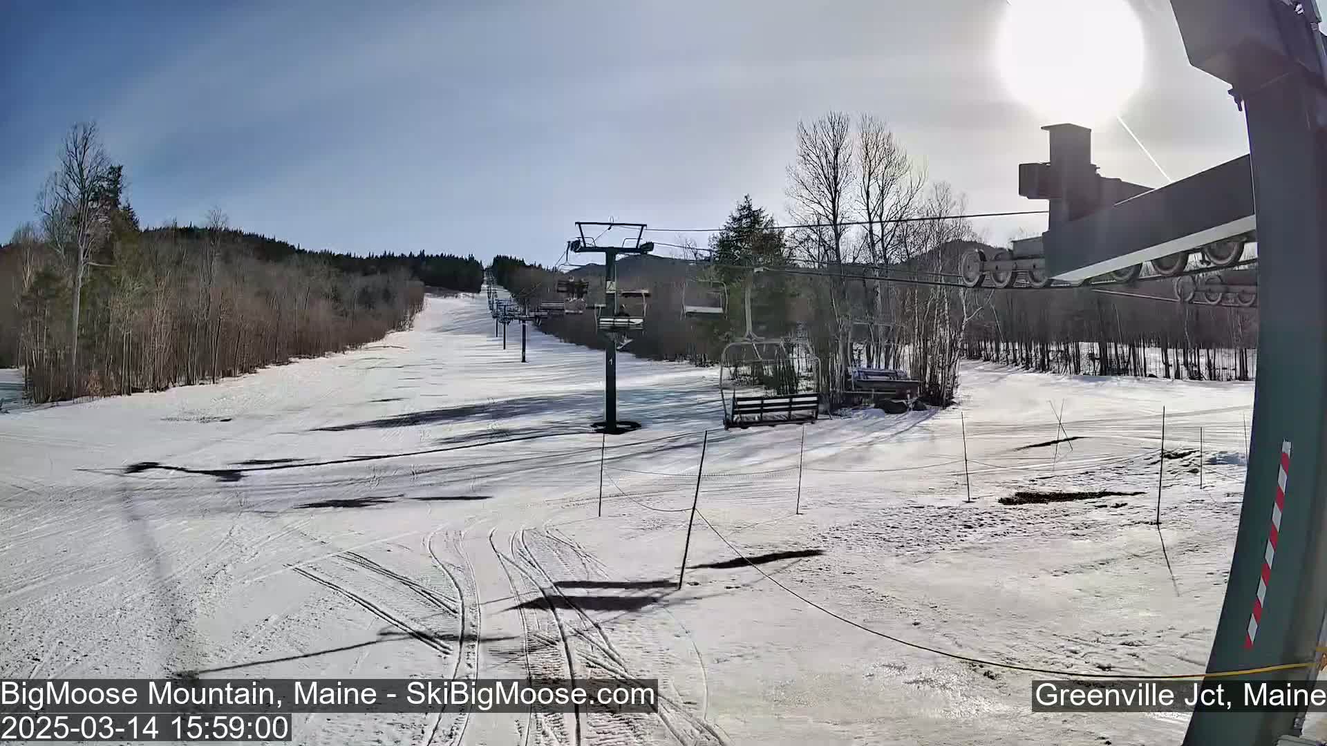 A sunny day at a snow-covered ski resort shows a chairlift and ski runs.