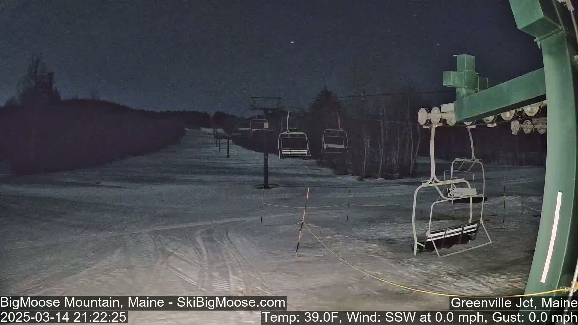 A nighttime view of a snow-covered ski slope with empty chairlifts under a dark sky.