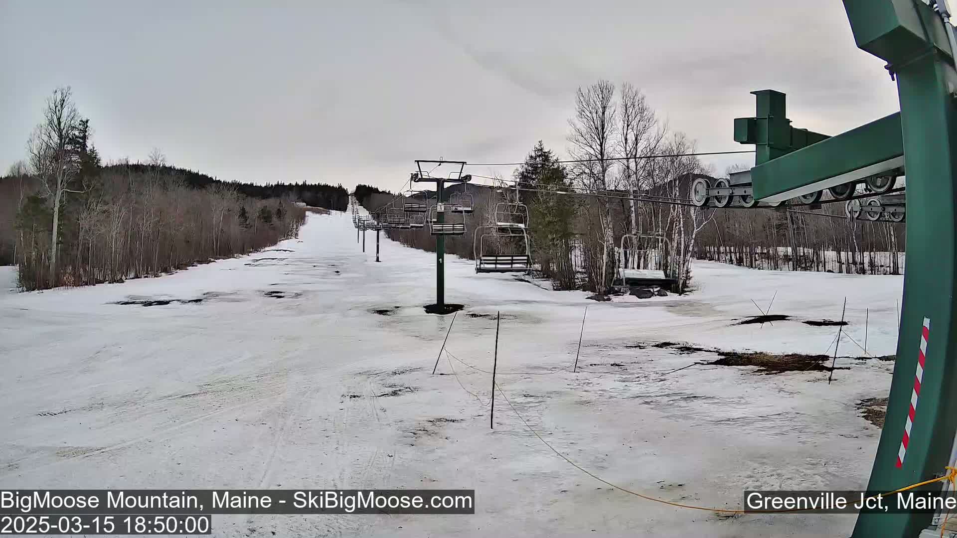 A snow-covered ski slope with a chairlift and bare trees under an overcast sky.