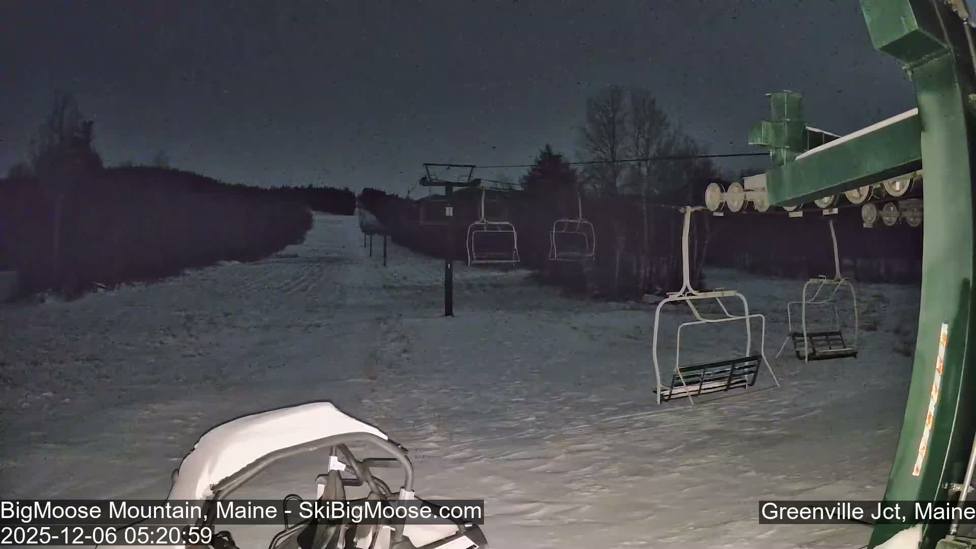 A snow-covered ski slope and empty chairlifts are visible in the dark, cold pre-dawn hours at a ski resort, under a hazy sky.