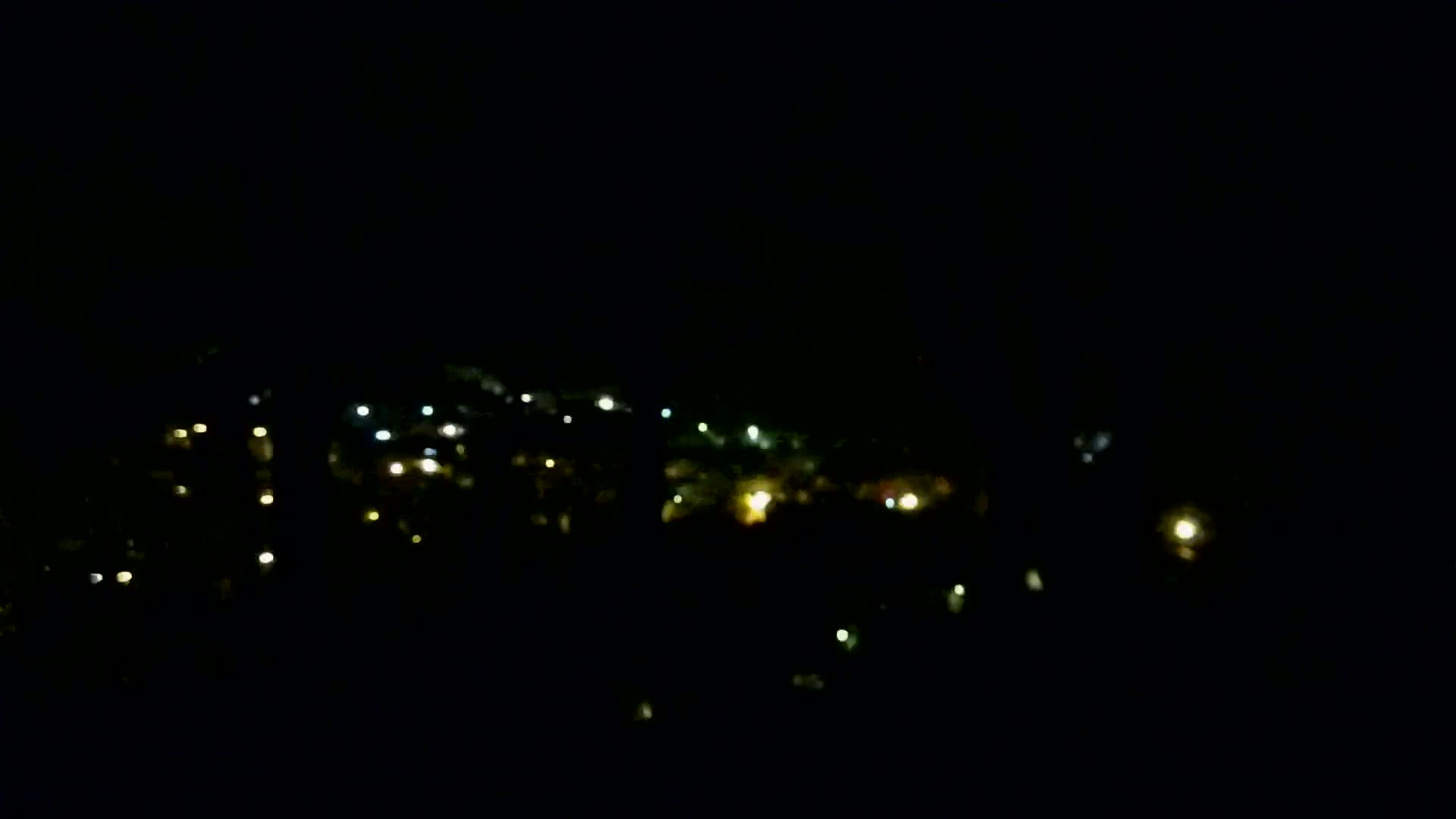 A blurry, nighttime view of scattered lights in a dark, possibly hilly, area.