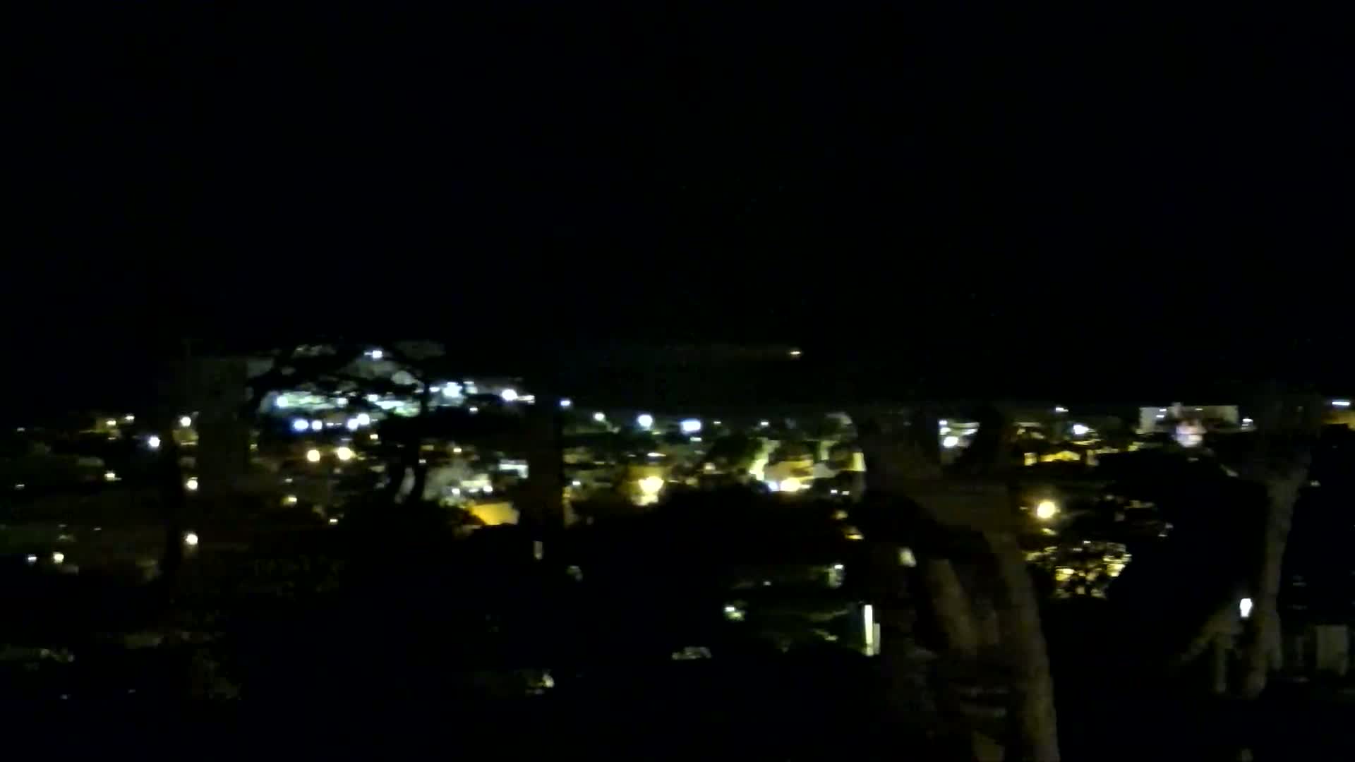 A nighttime view of a city's illuminated buildings and streets from a slightly elevated vantage point.