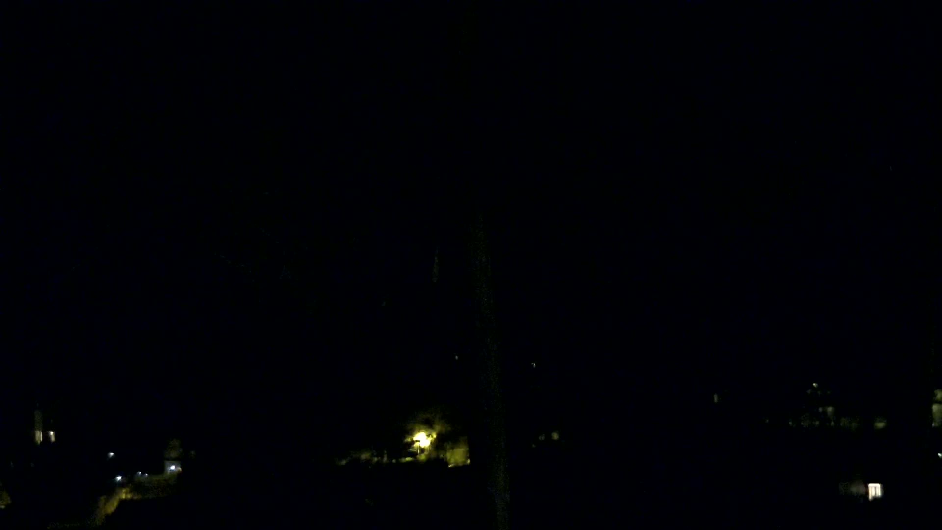 A dark nighttime scene shows faintly lit buildings and trees in the distance under a clear, black sky.