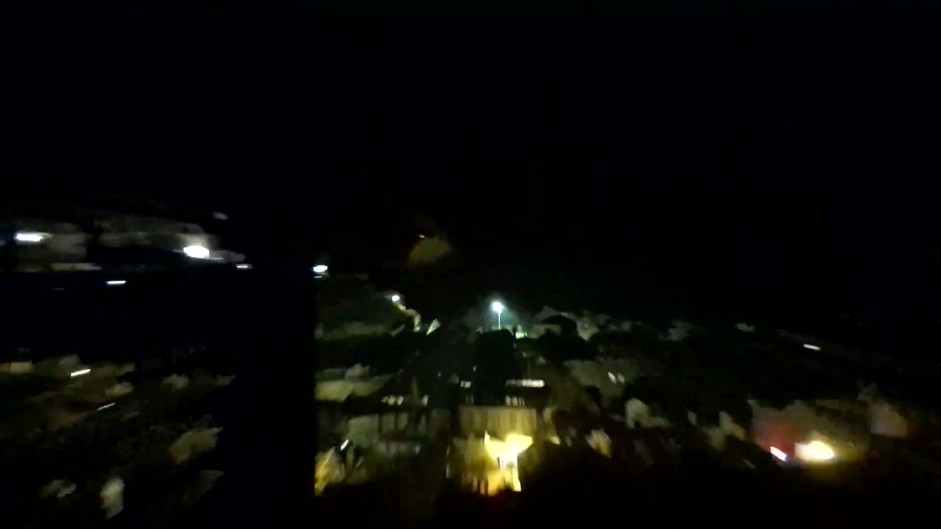 A nighttime aerial view shows a dimly lit town with scattered streetlights.